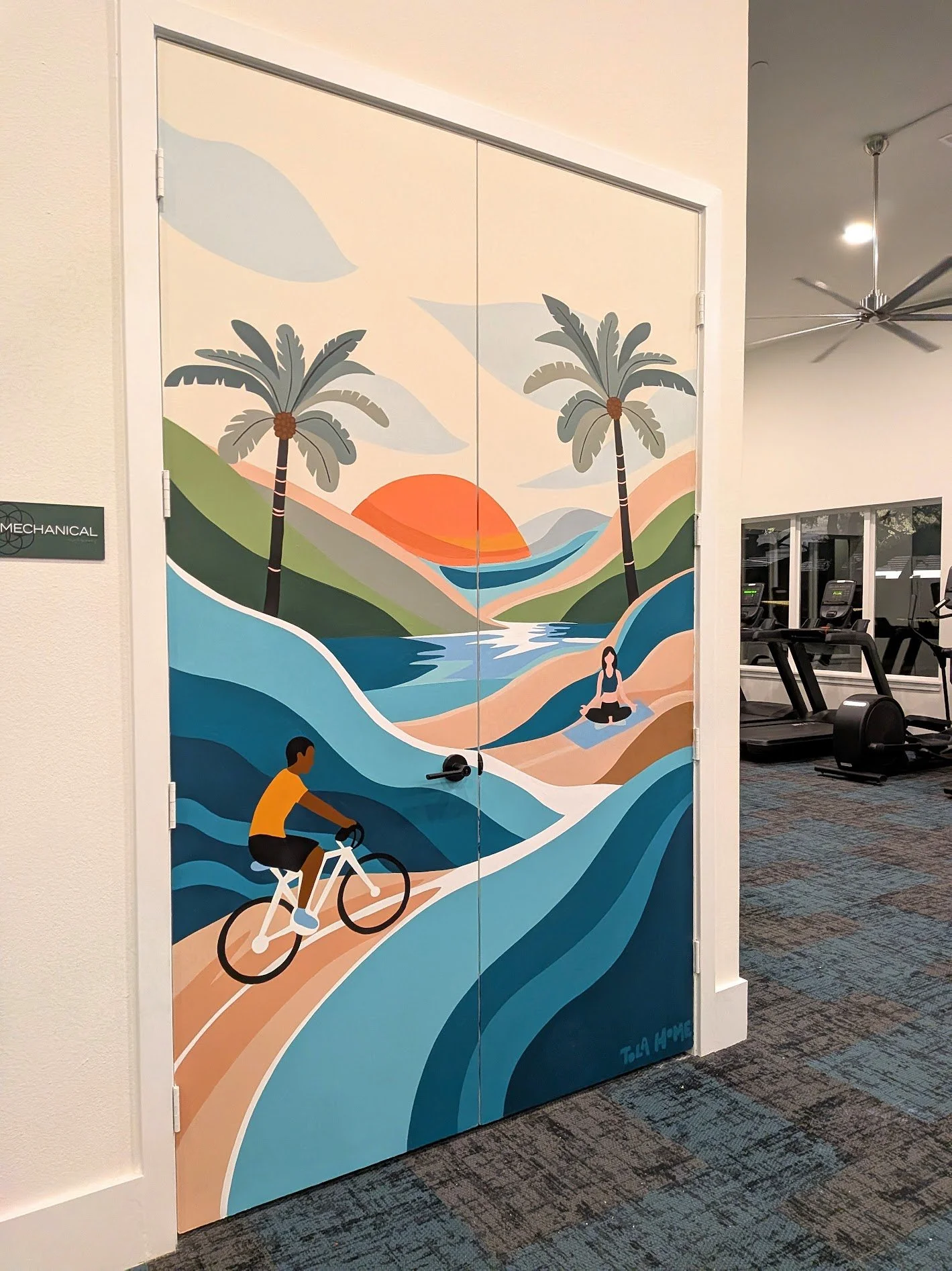 Fitness center mural in San Antonio featuring a cyclist, palm trees, mountains, and a sunset across a wall and door.