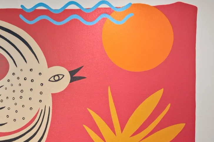 Colorful mural featuring a stylized bird with a patterned black and white body, an orange sun, blue waves, and yellow plant-like shapes on a red background.