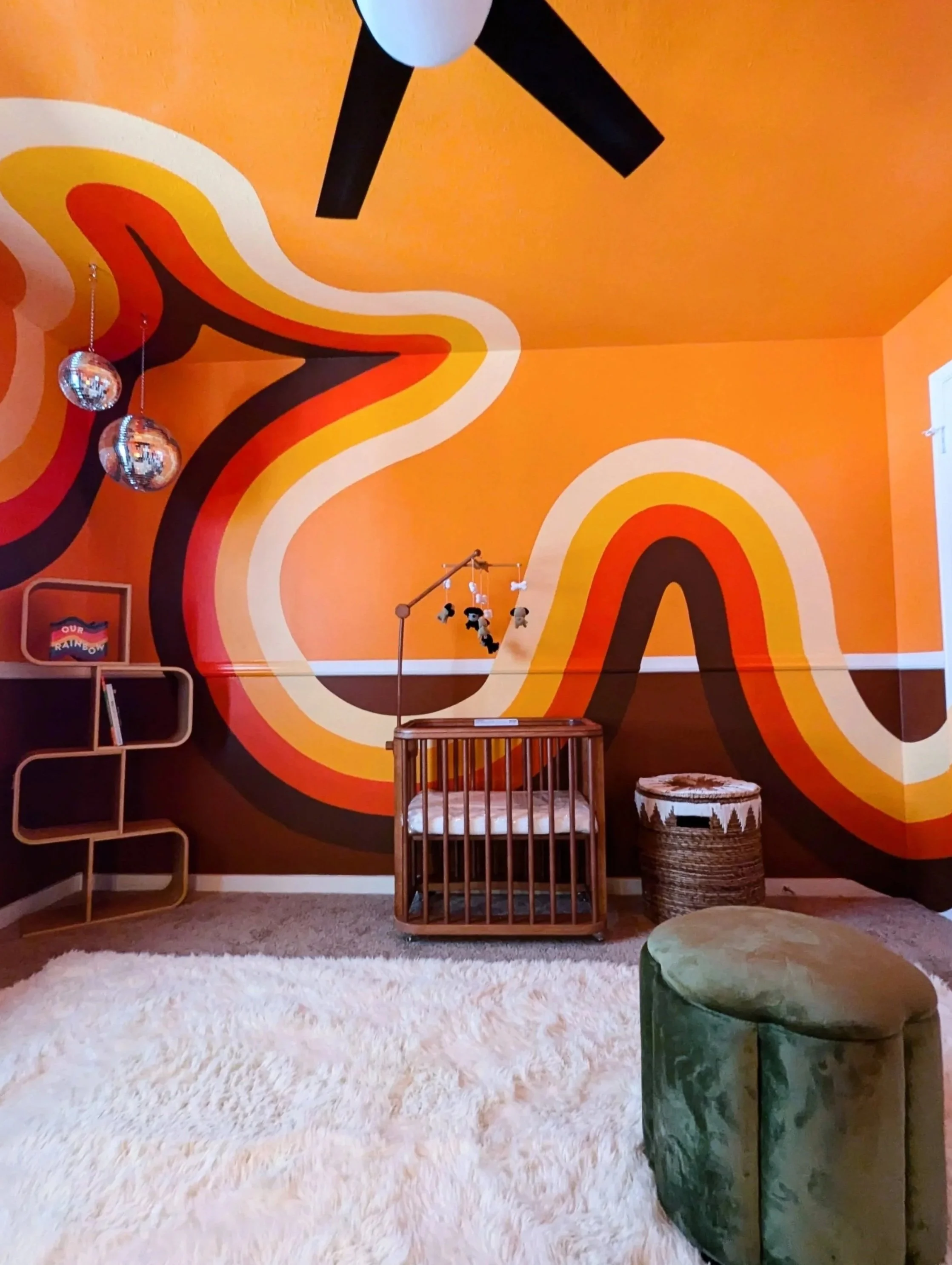 Retro nursery mural in Austin featuring an orange wave design spanning all four walls, ceiling, doors, and trim. Vintage furnishings, disco balls, and eclectic finds round out the room's interior design.