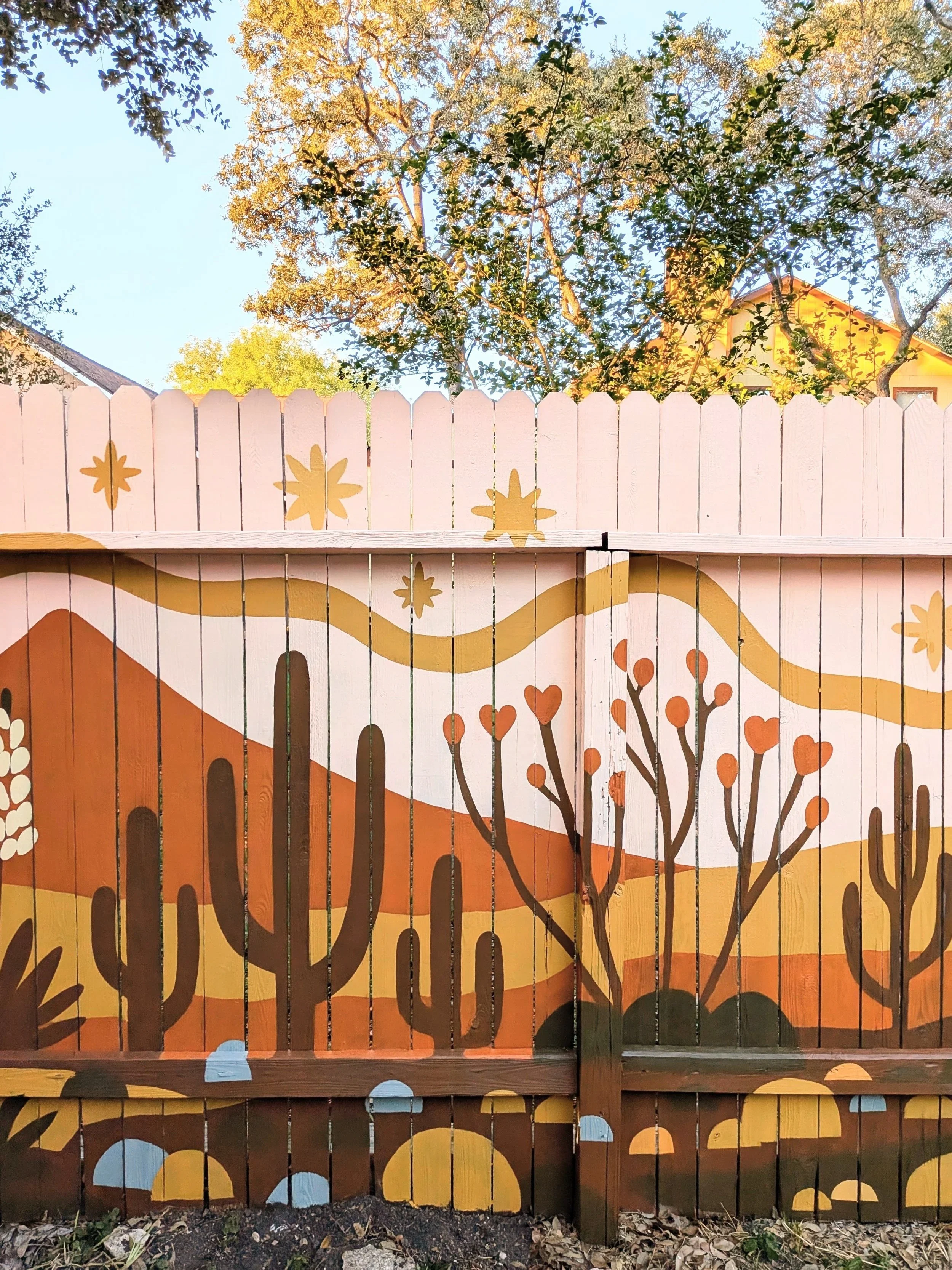 60-foot exterior fence mural for a San Antonio short-term rental featuring a pink and earth-toned desert landscape with cacti and native plants.