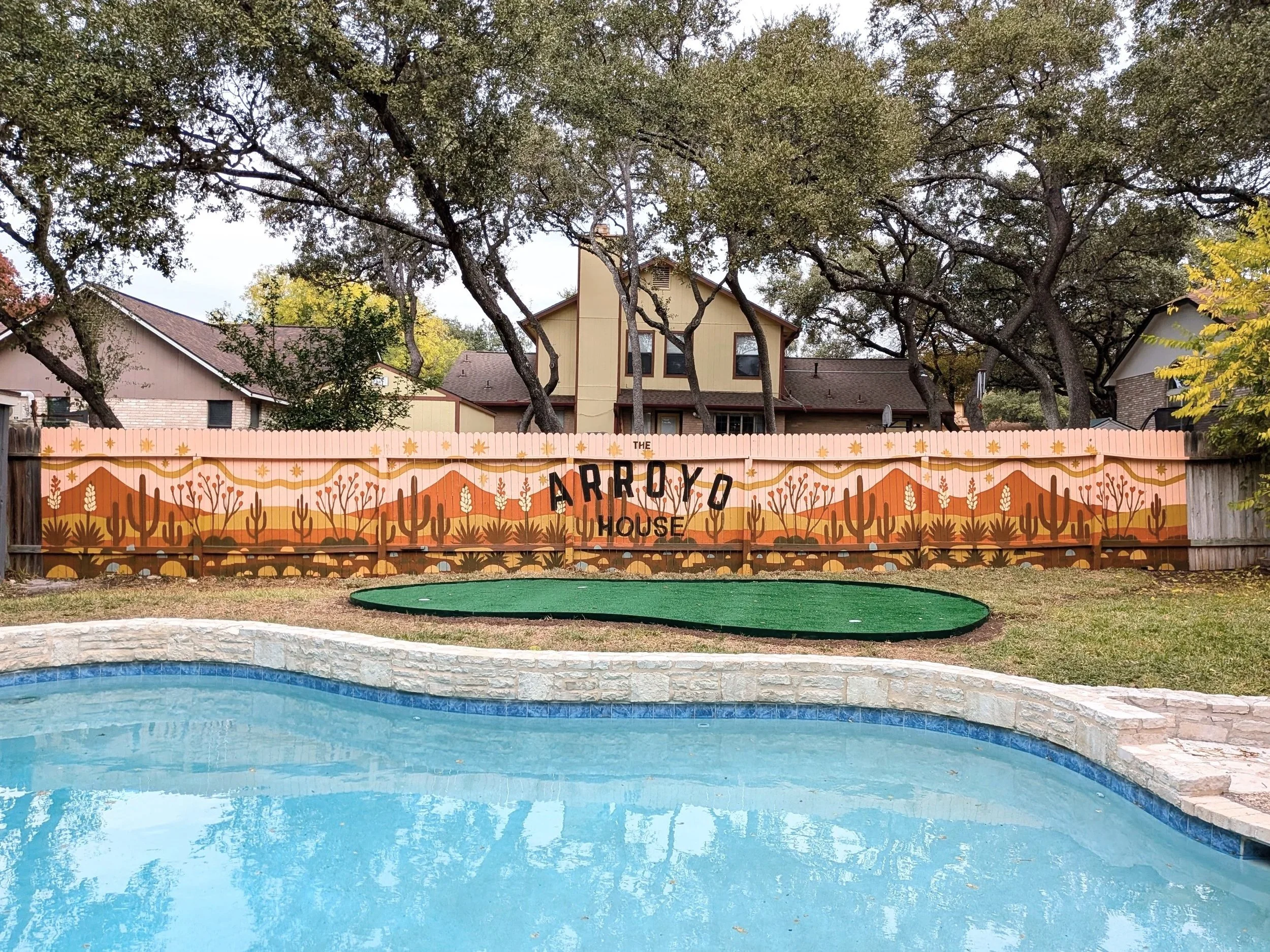 Exterior fence mural for a San Antonio short-term rental featuring pink desert hills, cacti, native plants, and earth-toned landscape forms.