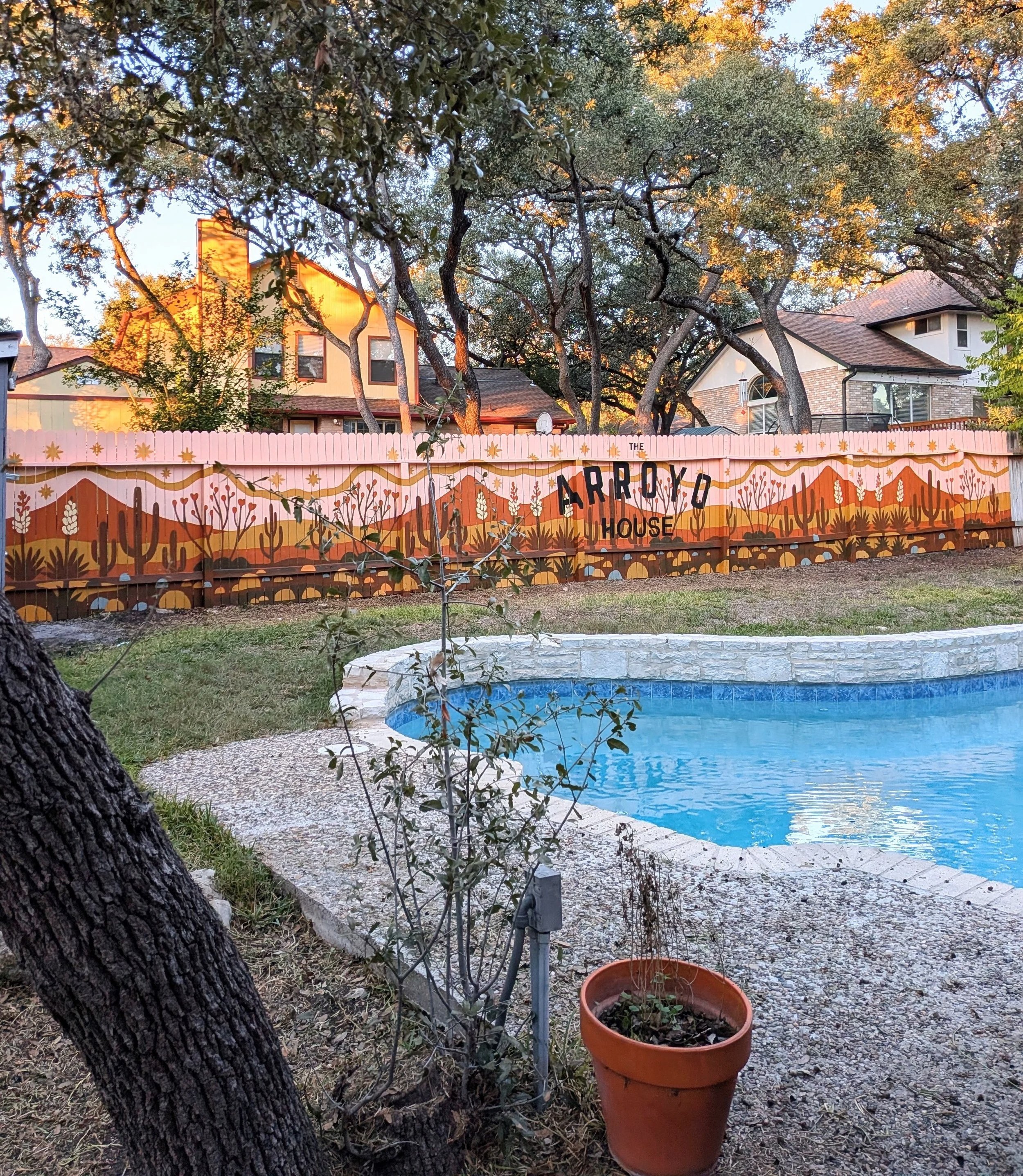 Arroyo House exterior mural in San Antonio featuring property branding centered within a 60-foot painted desert landscape fence overlooking a backyard pool. 