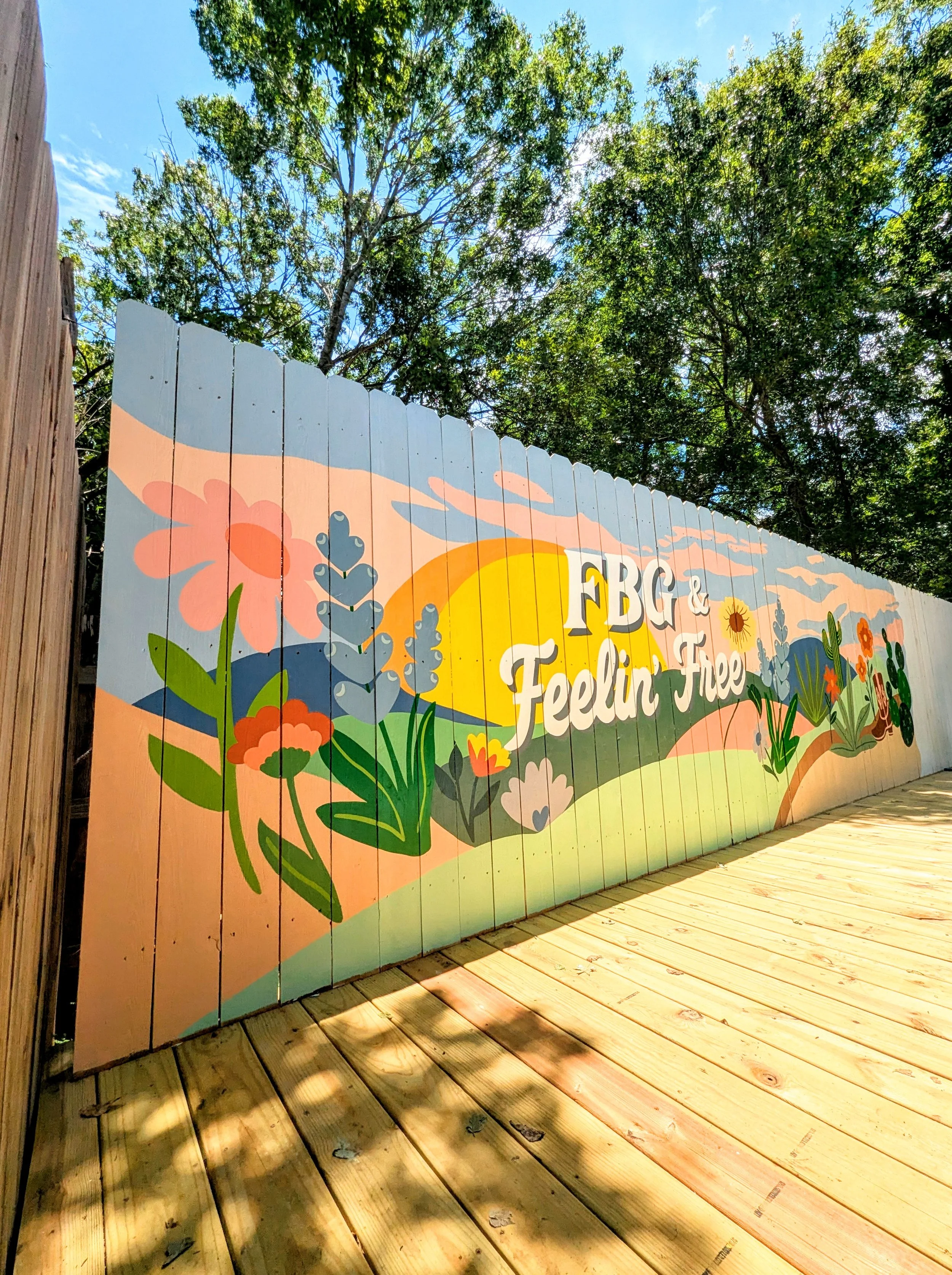Fredericksburg, Texas short-term rental mural featuring a painted fence with wildflowers, Texas hill country, and a sunset landscape.