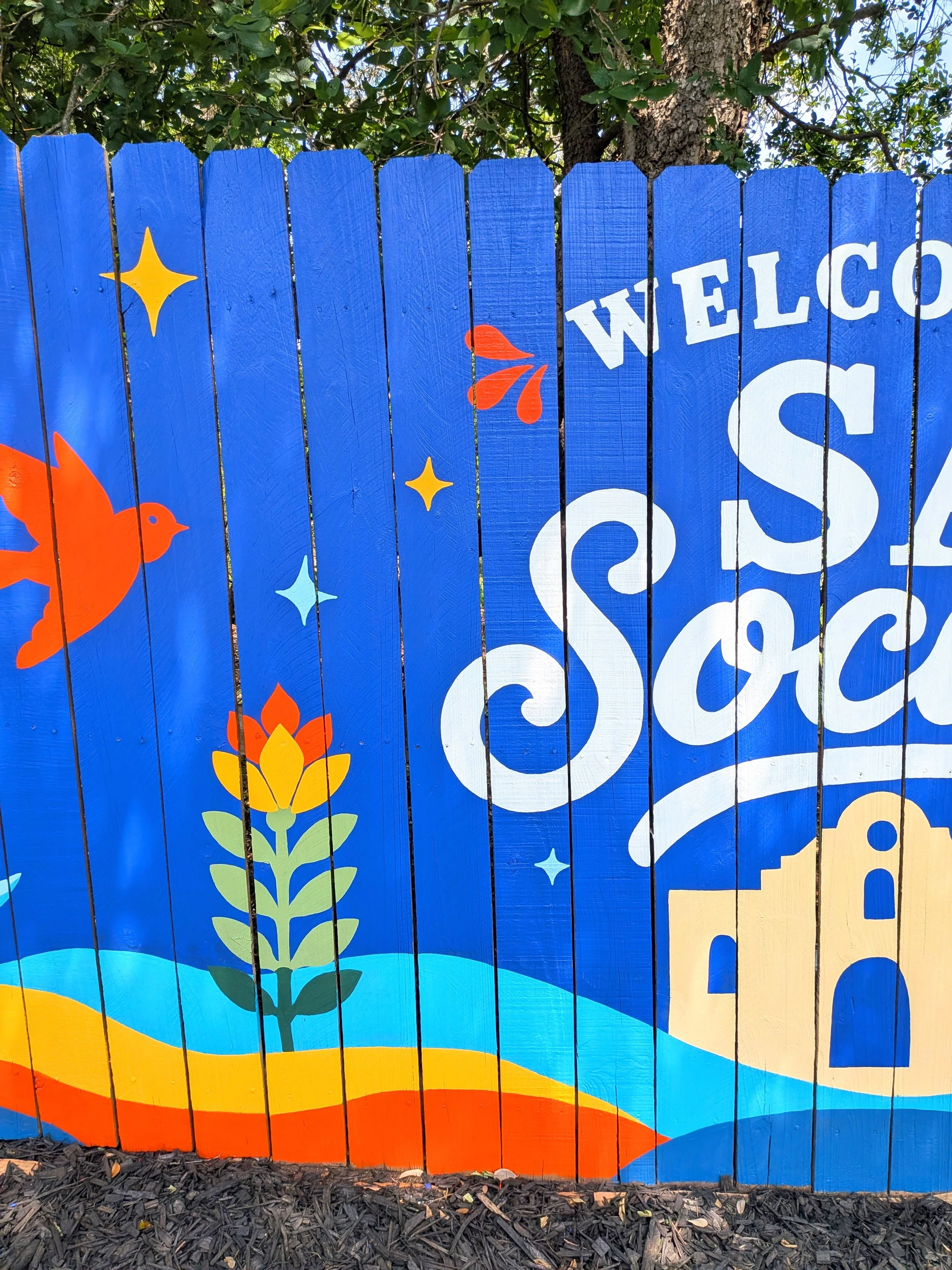 San Antonio short-term rental exterior mural featuring "SA Social Club" decorative typography, colorful flowers, birds, and Texas-inspired landscape