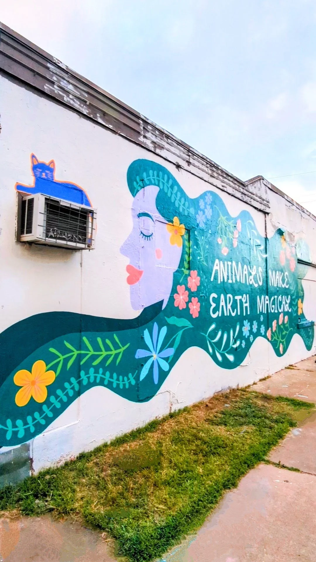 Large-scale Austin Pets Alive! mural in Austin, Texas featuring a woman's profile, Texas native flowers, greenery, and the phrase "Animals Make Earth Magical."