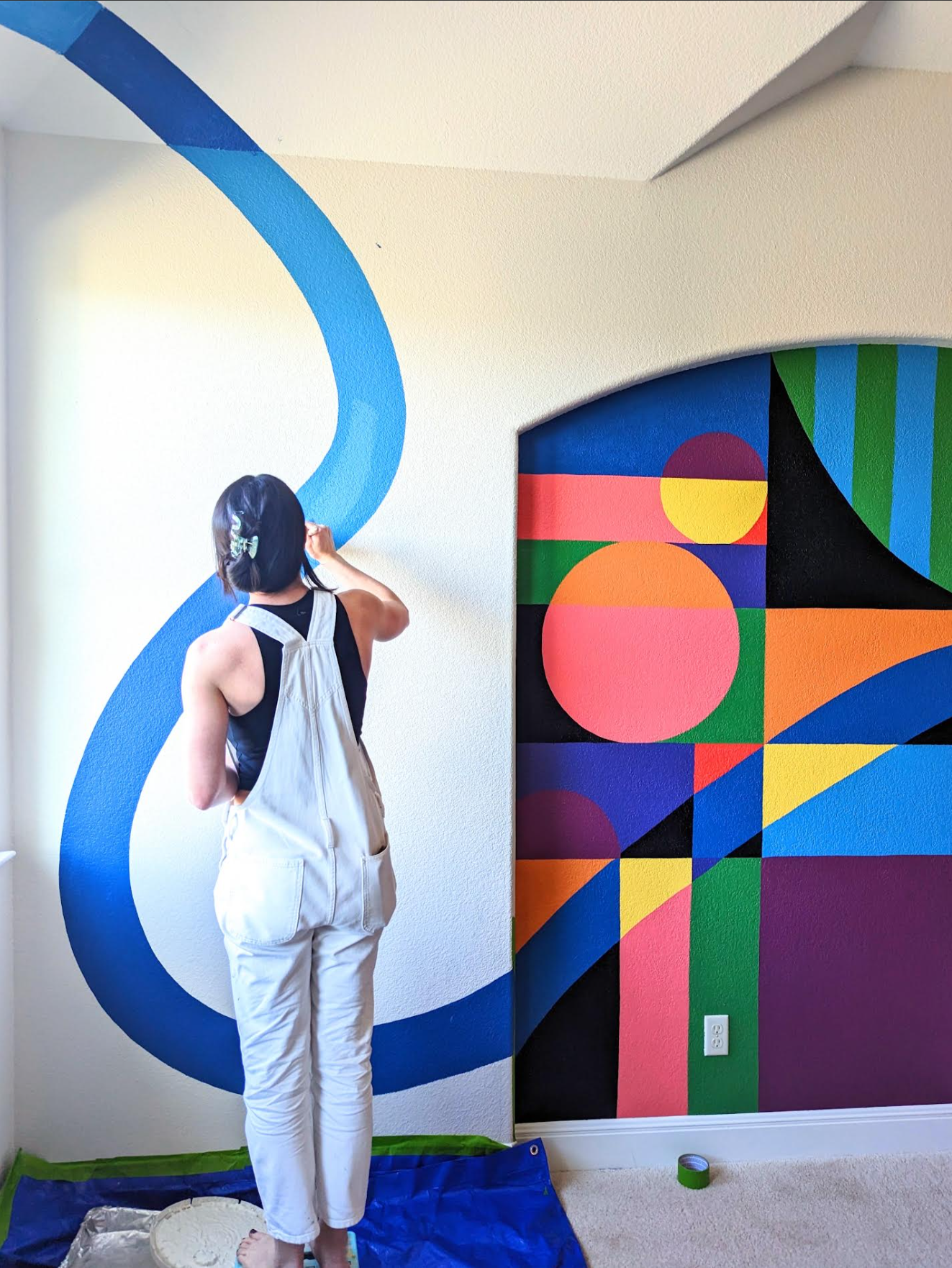 Tola Home painting a colorful geometric mural in a kid's playroom.