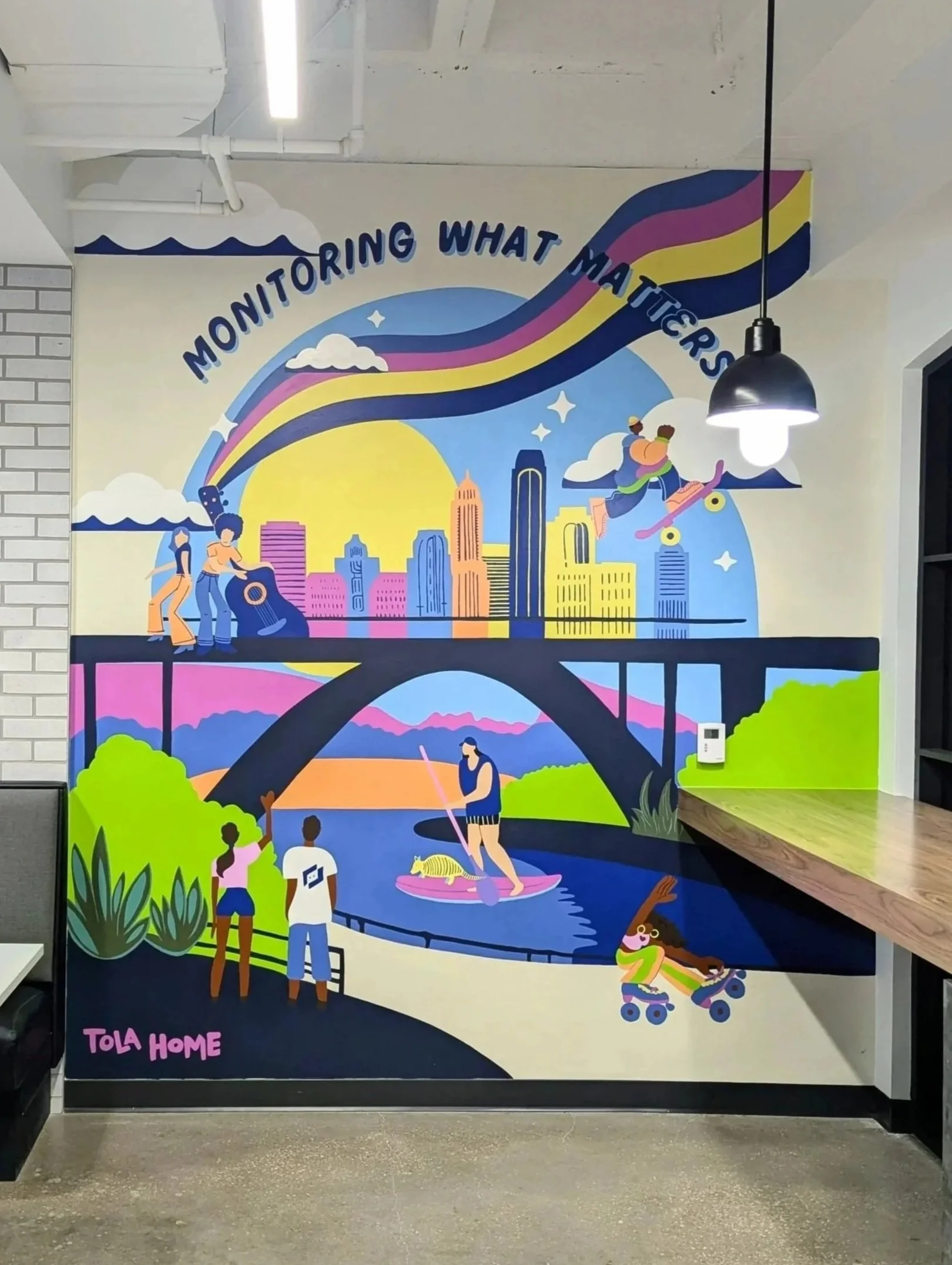 LogicMonitor office mural in Austin featuring a colorful cityscape, outdoor activities, and the company's “Monitoring What Matters” message using LongMonitor's brand colors.