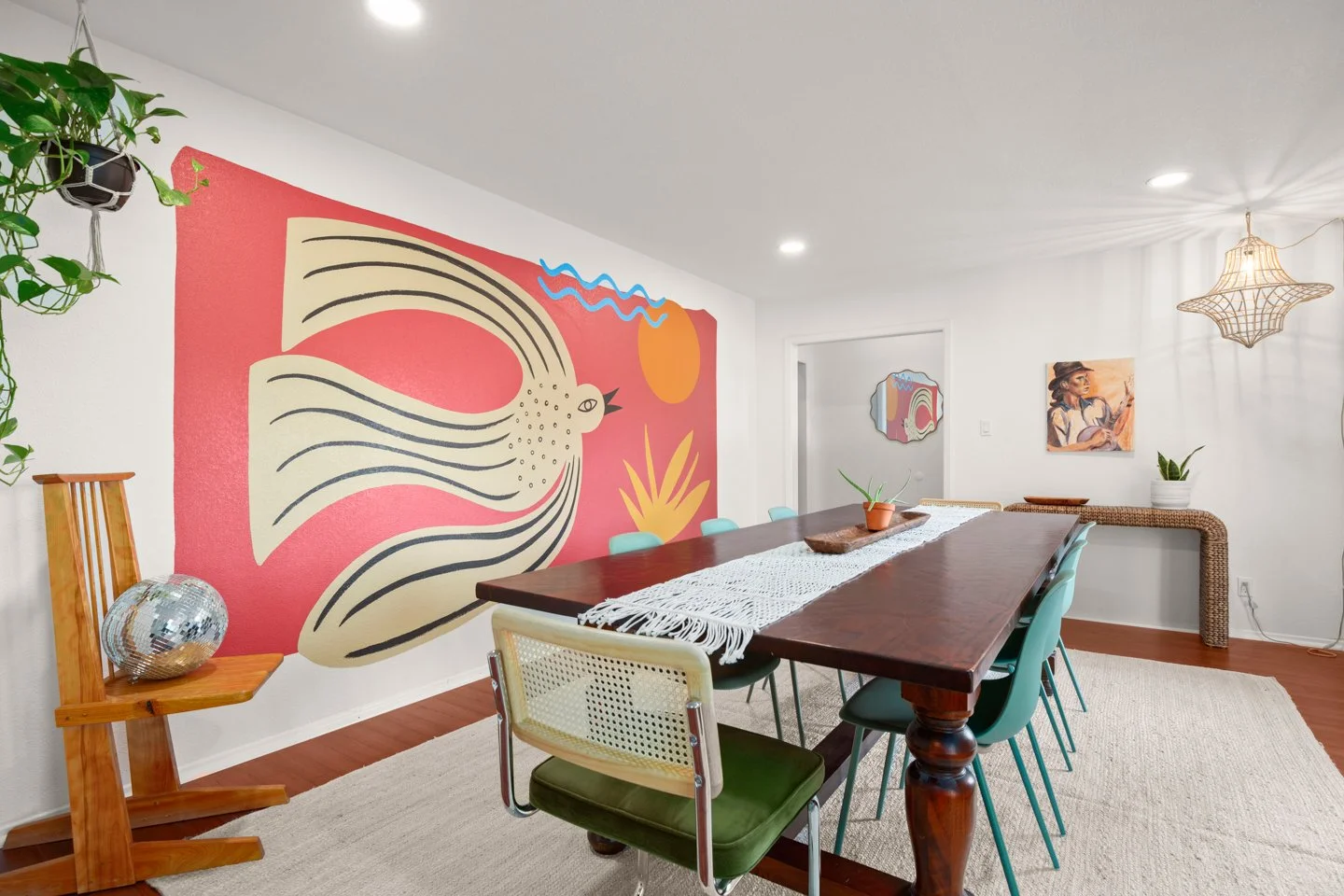 Original artwork by Tola Home featuring a folk art style bird, sun, waves, and botanical shapes in a colorful, earthy dining room.