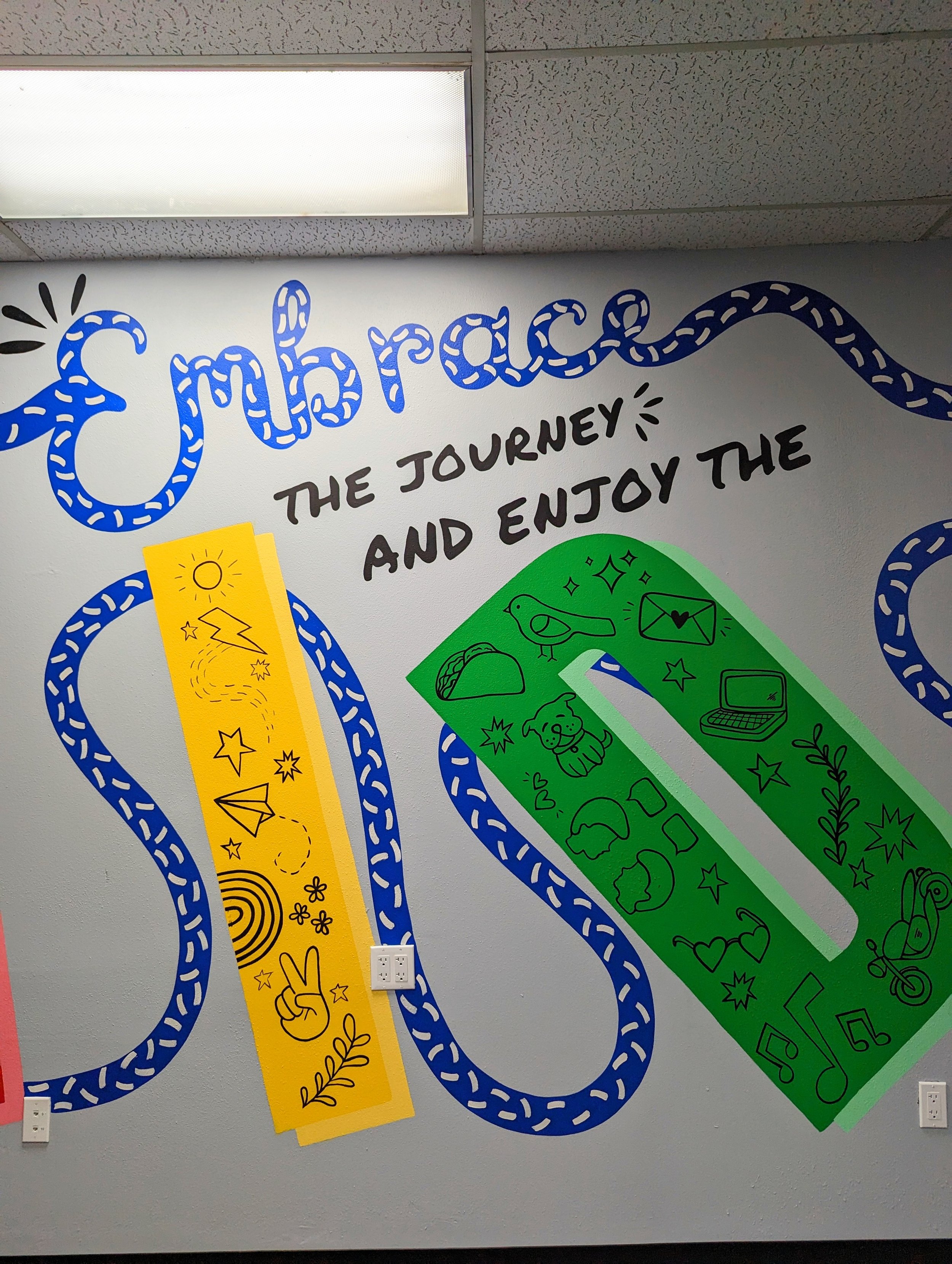 Decorative wall art with the phrase 'Celebrate the journey and enjoy the ride' and colorful symbols such as a yellow lightning bolt, a green sneaker, and music notes.