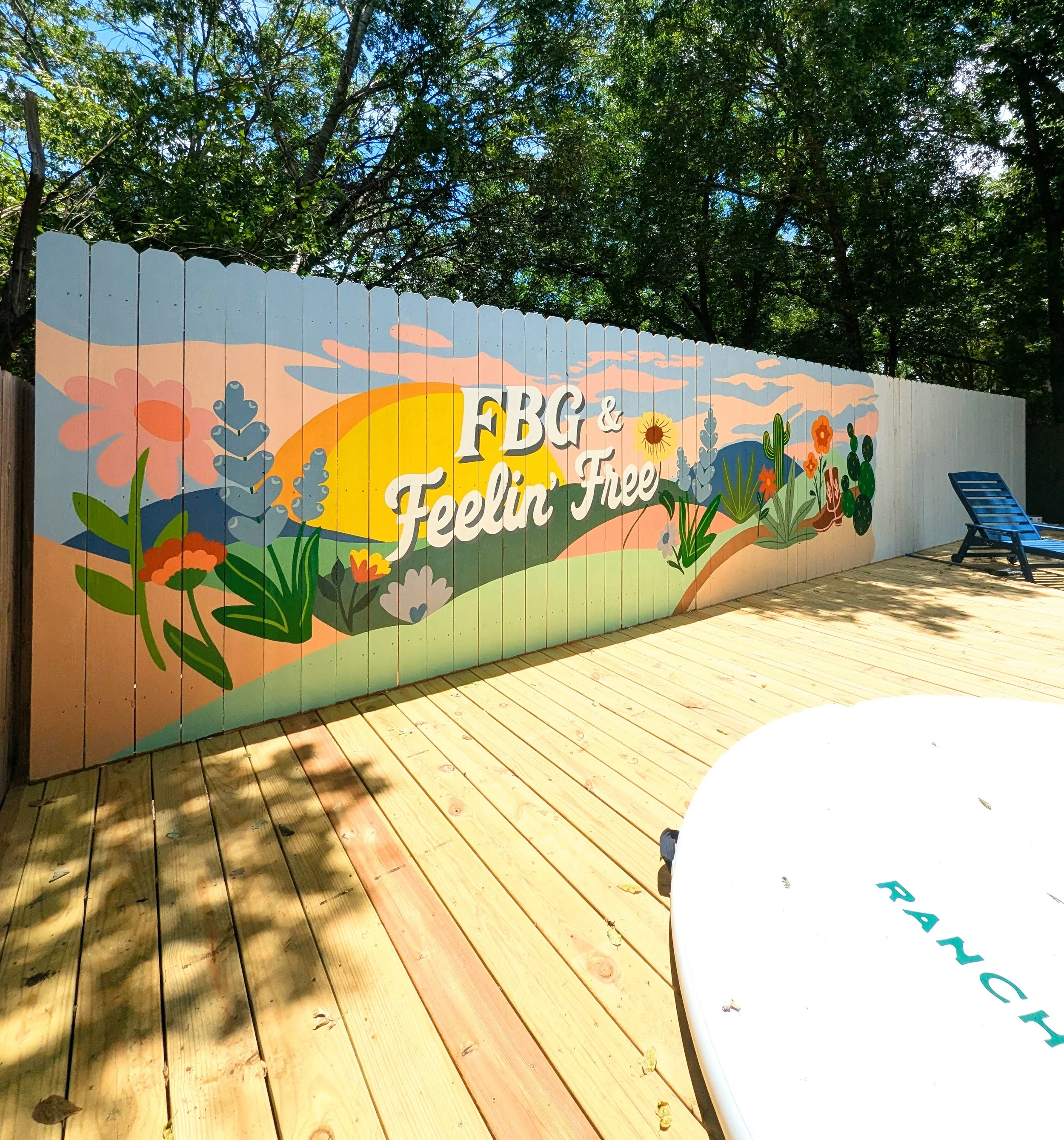 Fredericksburg, Texas short-term rental mural featuring a painted outdoor fence with desert plants, rolling Texas hills, native flowers, and a sunset landscape.