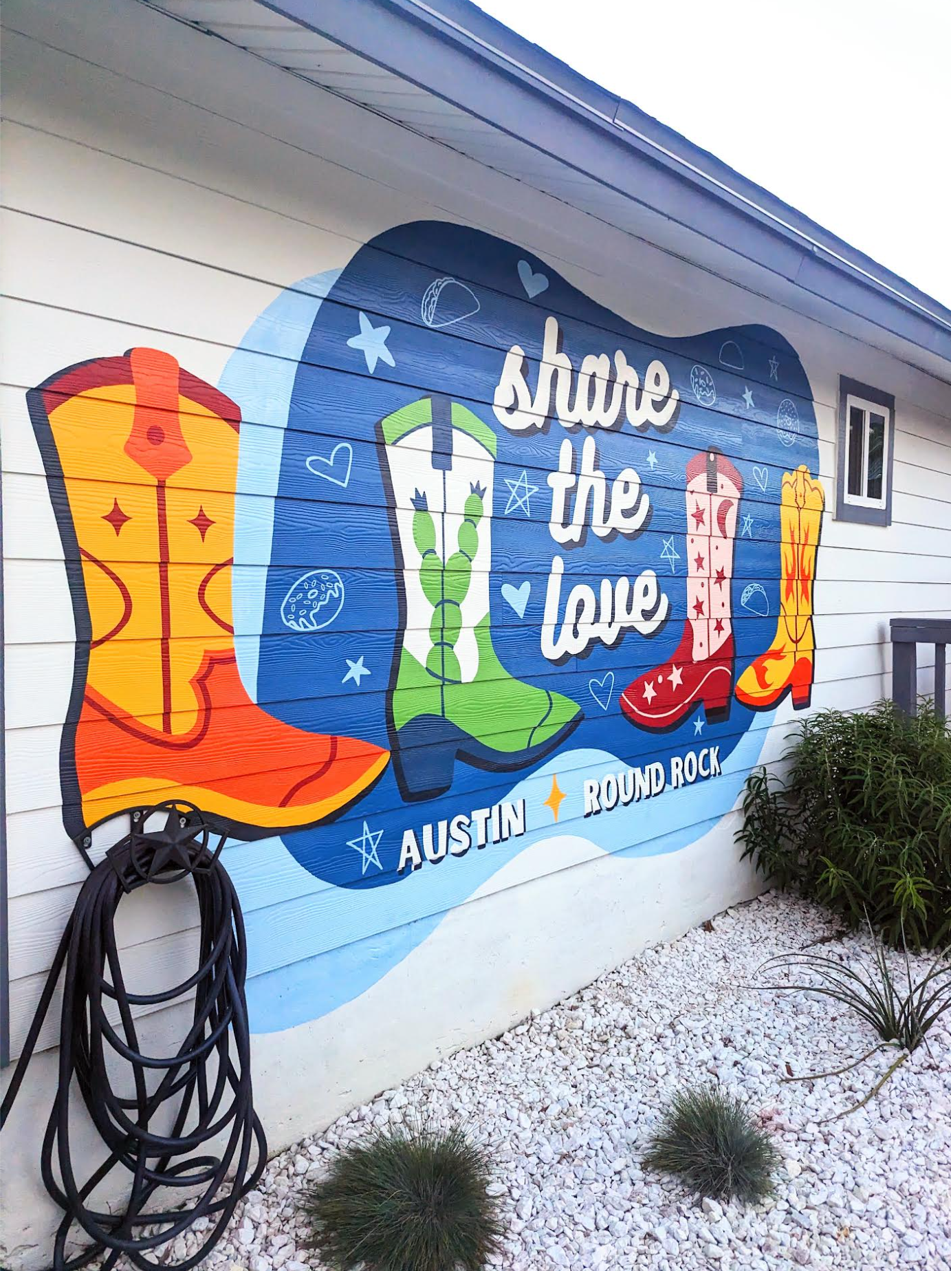 Colorful exterior mural on the side of a building promoting the bond between Austin, TX and Round Rock, TX, with the phrase 'Share the Love' and decorative stars, hearts, and tacos.