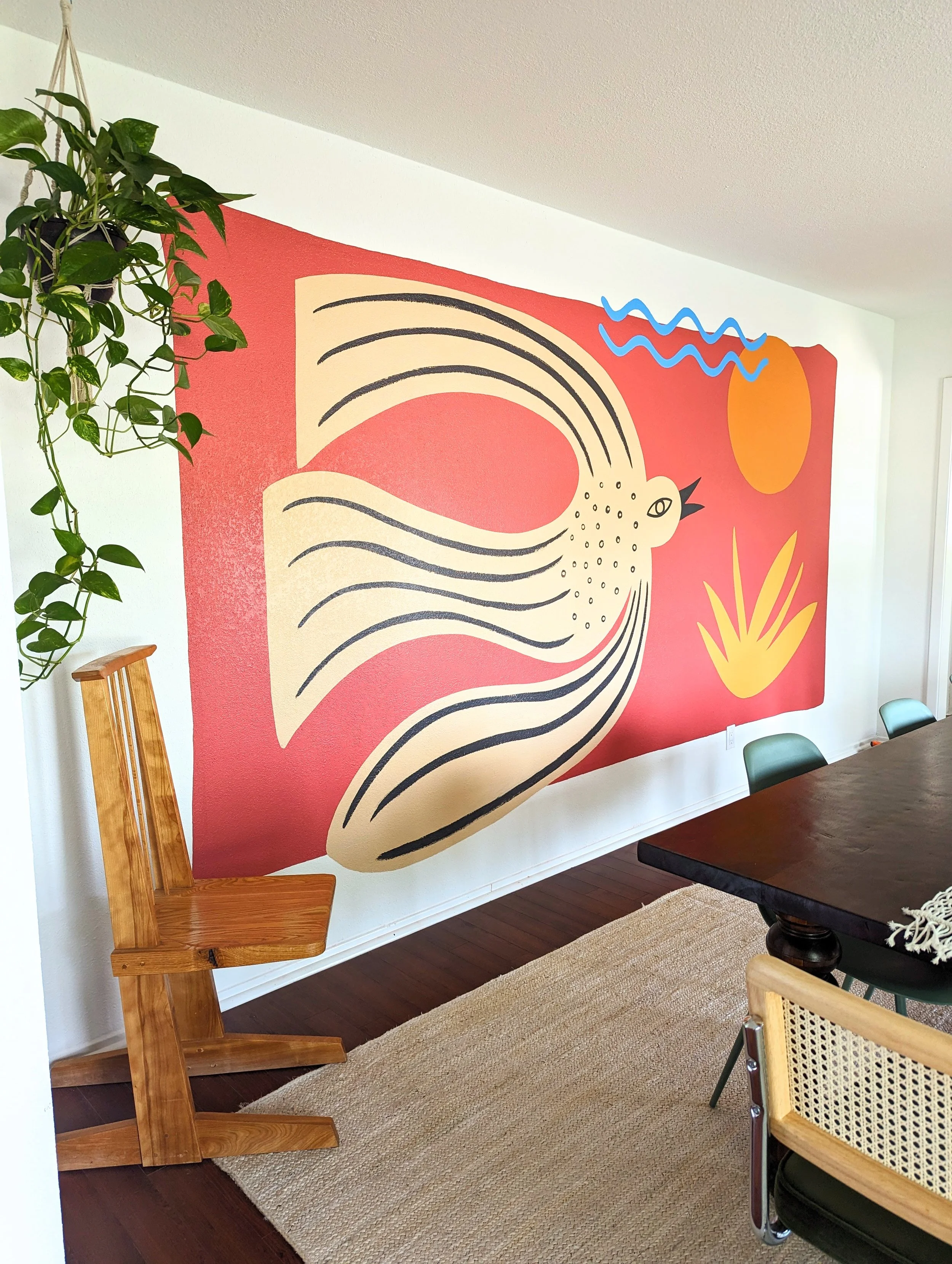 Original mural by Tola Home featuring a folk art style bird, sun, waves, and botanical shapes in a colorful, earthy dining room.