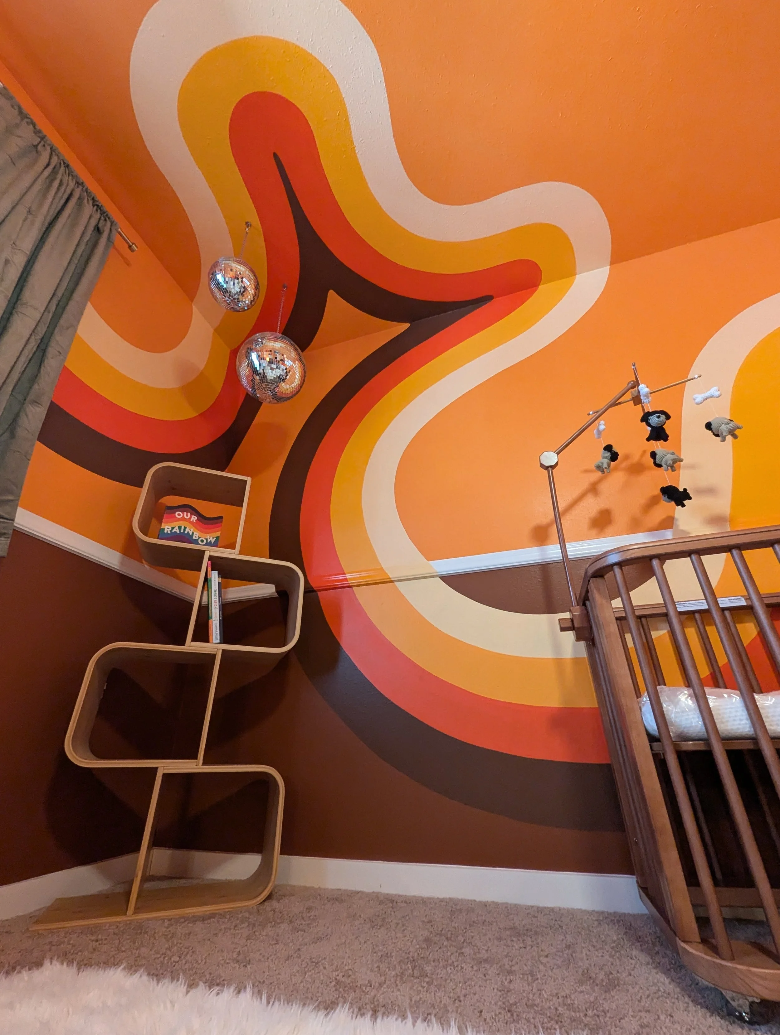 Retro nursery interior design in Austin featuring an orange wave mural, vintage furnishings, hanging disco balls, and eclectic decor.