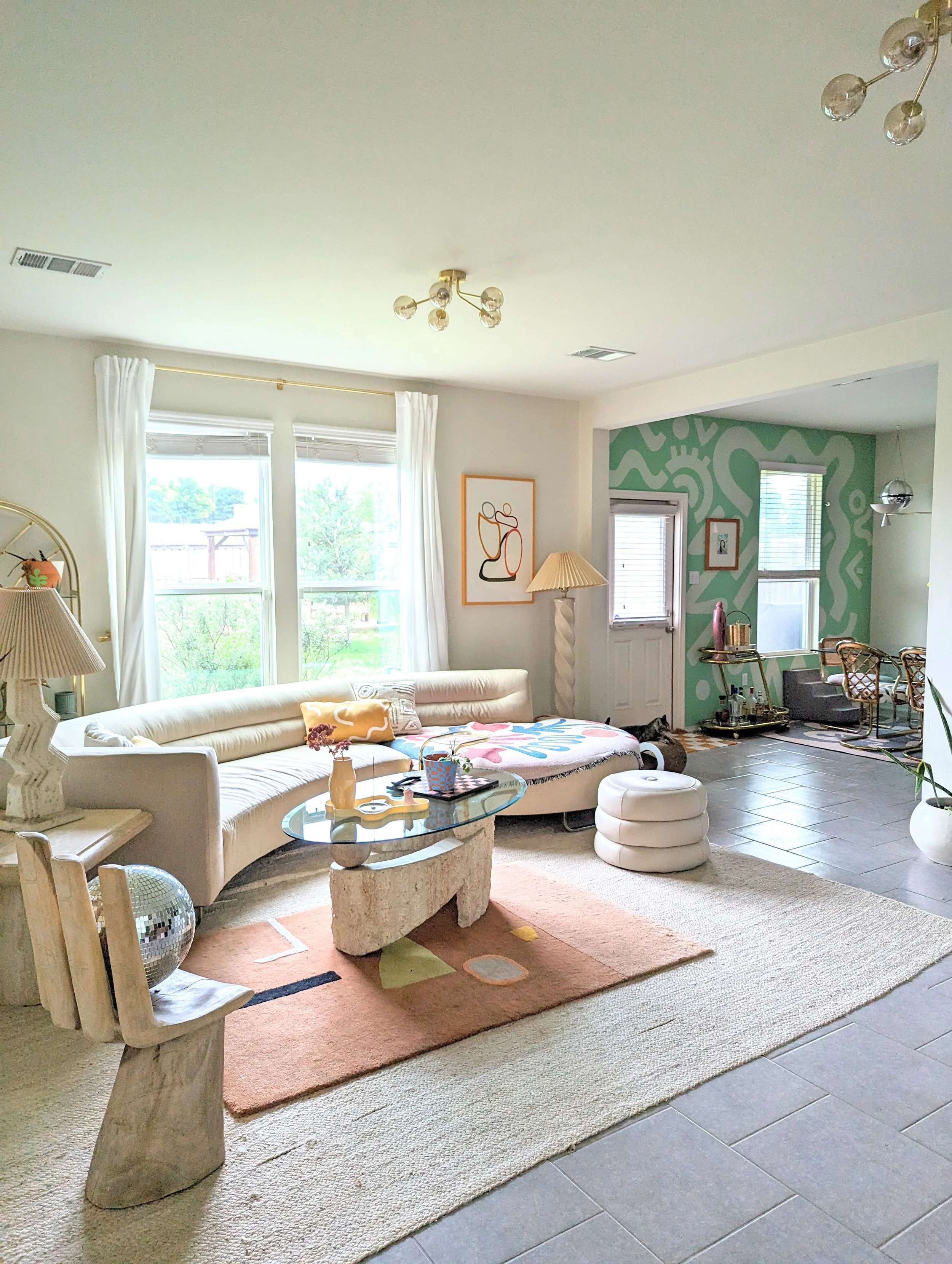 Eclectic living room in an Austin-area home featuring vintage furnishings, original artwork, patterned wallpaper, and layered textiles, featured in Apartment Therapy.