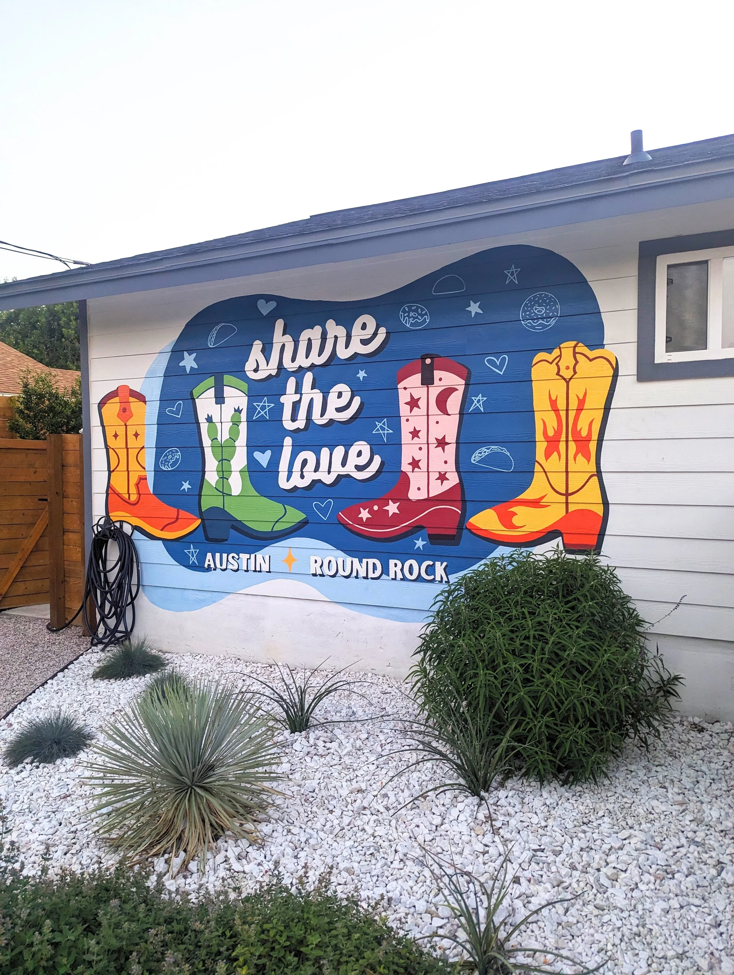 A Round Rock short-term rental mural with the phrase "share the love" on the side of a house, featuring illustrations of cowboy boots, stars, and hearts. 