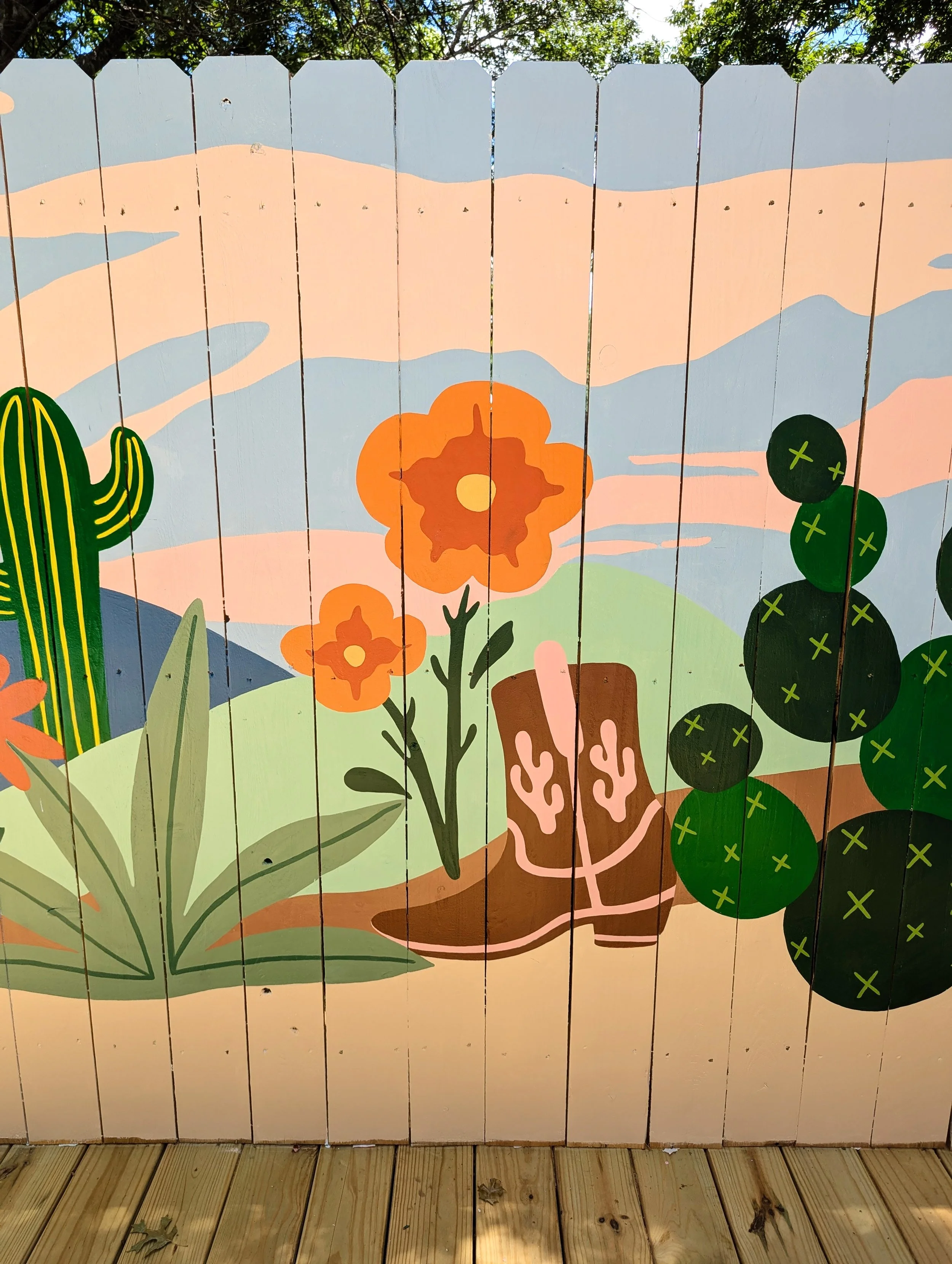 Fredericksburg, Texas short-term rental fence mural featuring Texas Hill Country-inspired landscape, cacti, wildflowers, and clouds.