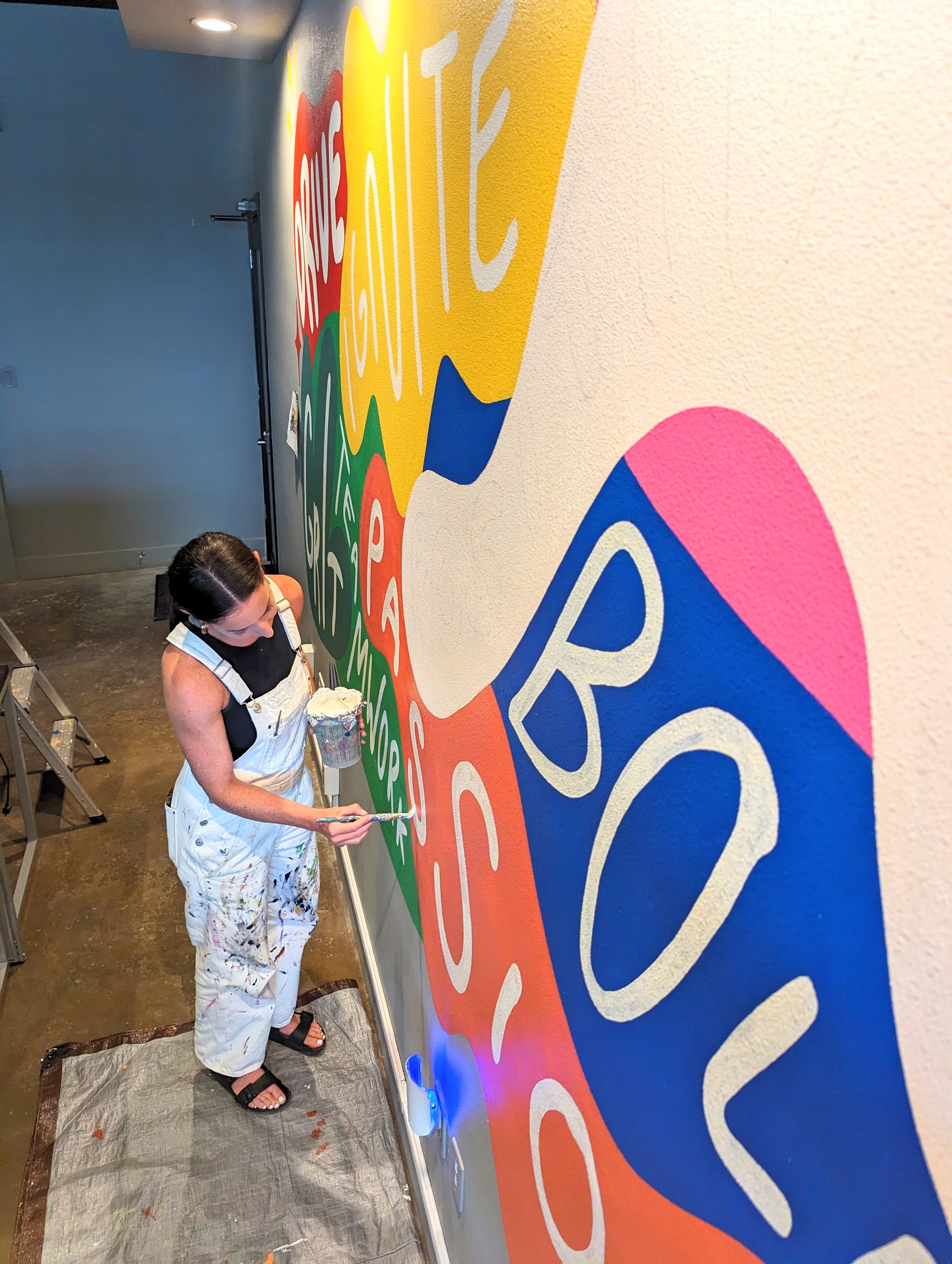 Centex Auto Title office mural in Austin showing the artist painting colorful Texas-inspired artwork with bold typography and graphic imagery.