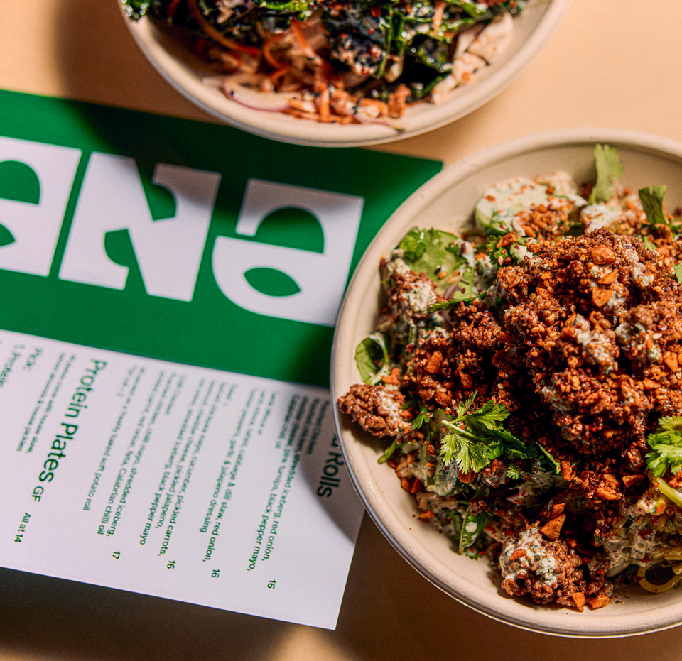 SANA MEDITERRANEAN sydney. Two bowls of Asian-inspired salads with ground meat, fresh vegetables, and herbs, placed on a table with a green and white Takeout menu.