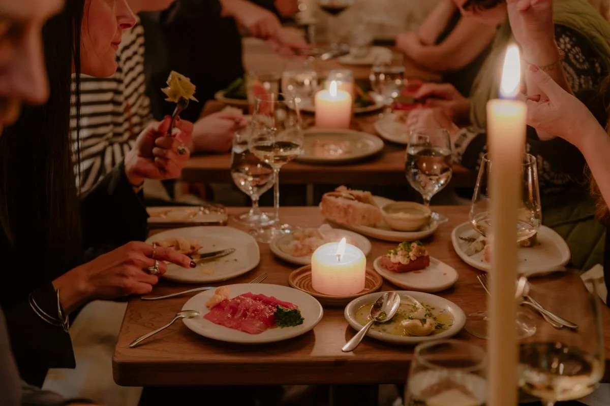 People gathered around a dinner table enjoying a meal with candles and wine glasses.