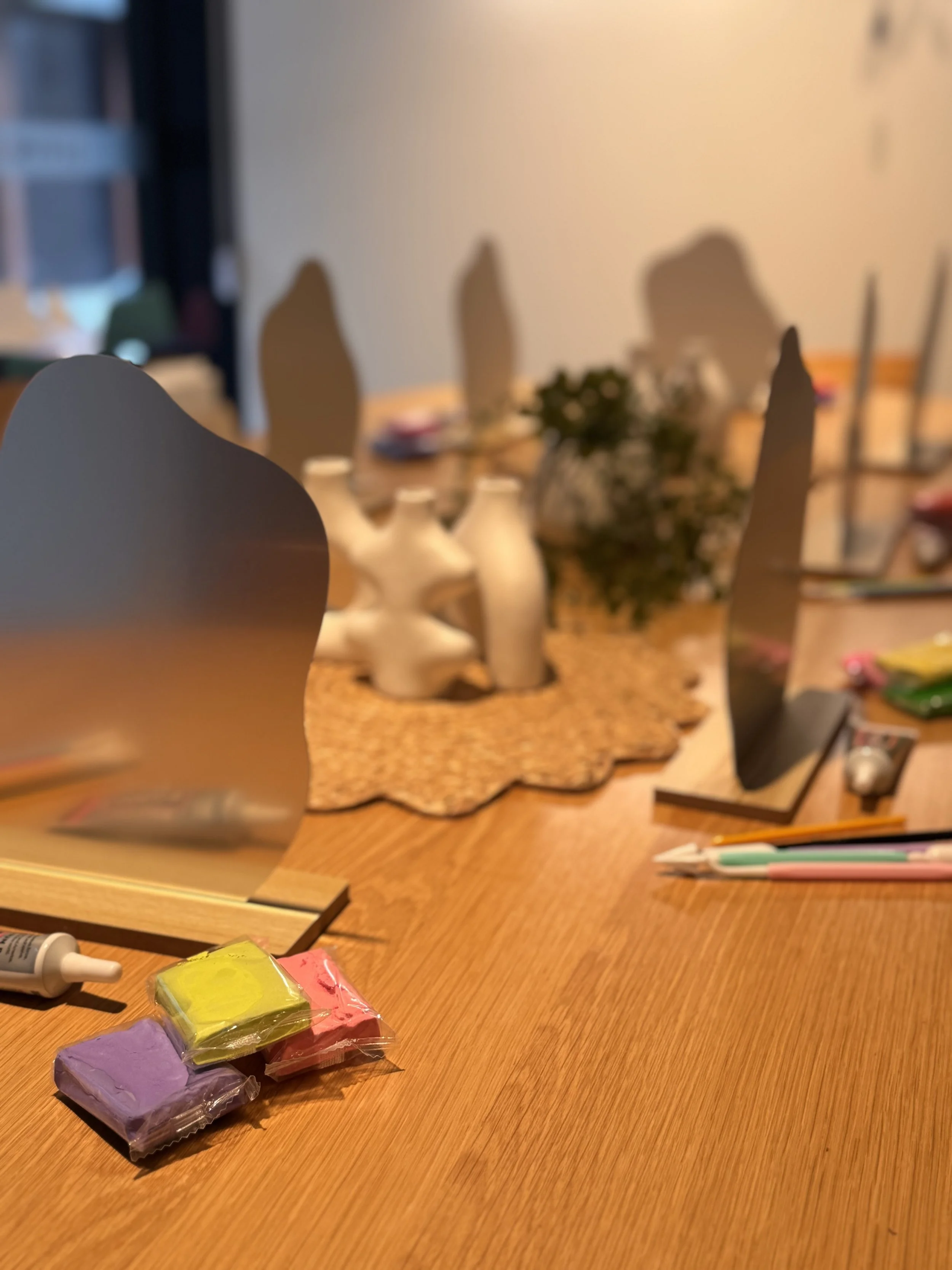 Colorful modeling clay blocks on a wooden table, with a background of chairs, a plant, and art supplies. kids soiree air clay party