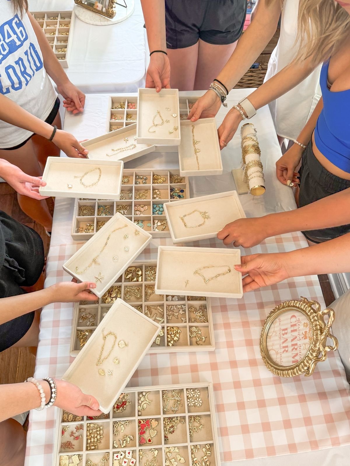 Multiple people shopping for jewelry at a market stall with trays of gold necklaces, bracelets, earrings, and rings on a checkered tablecloth. kids soiree craft activity parties