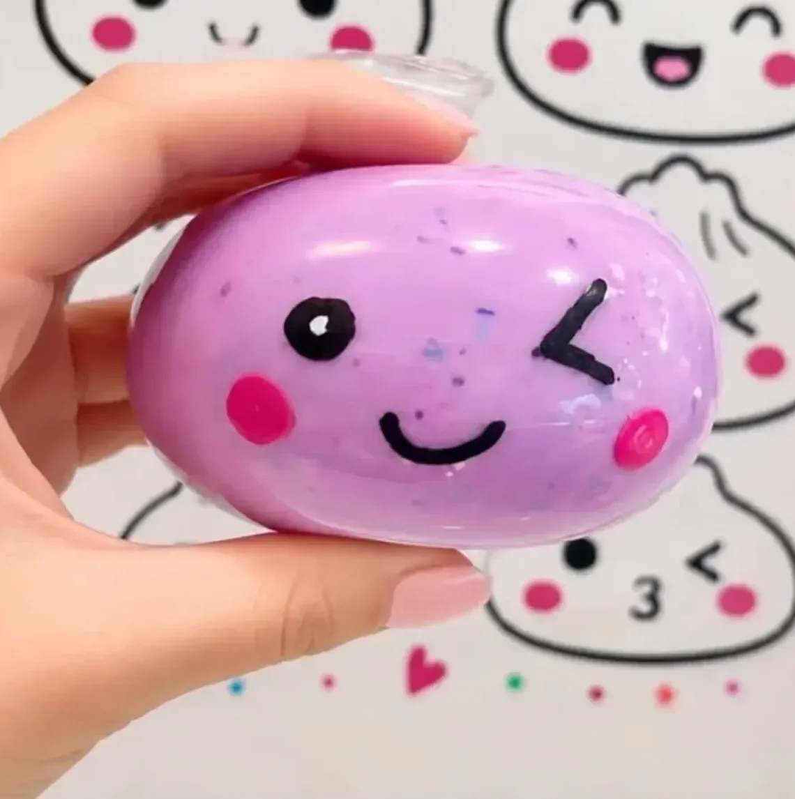Purple oval-shaped stone decorated with a kawaii-style face, including a winking eye, a smiling mouth, and pink cheeks. kids soiree craft activity parties