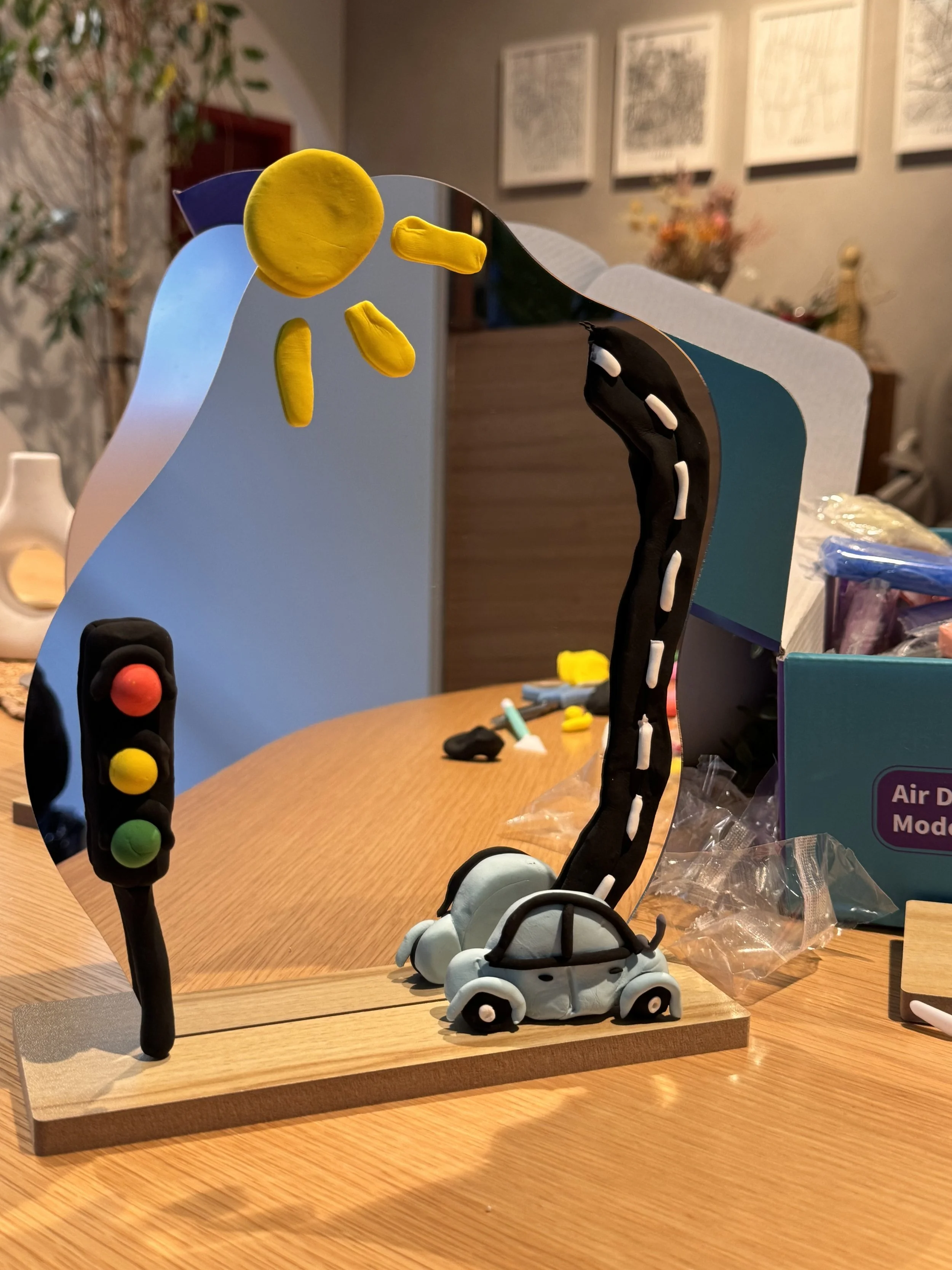 Miniature models of traffic lights, a person crossing signal, and a skateboard with a dog figure, all made from colorful clay or similar material, displayed on a wooden base.kids soiree air clay party