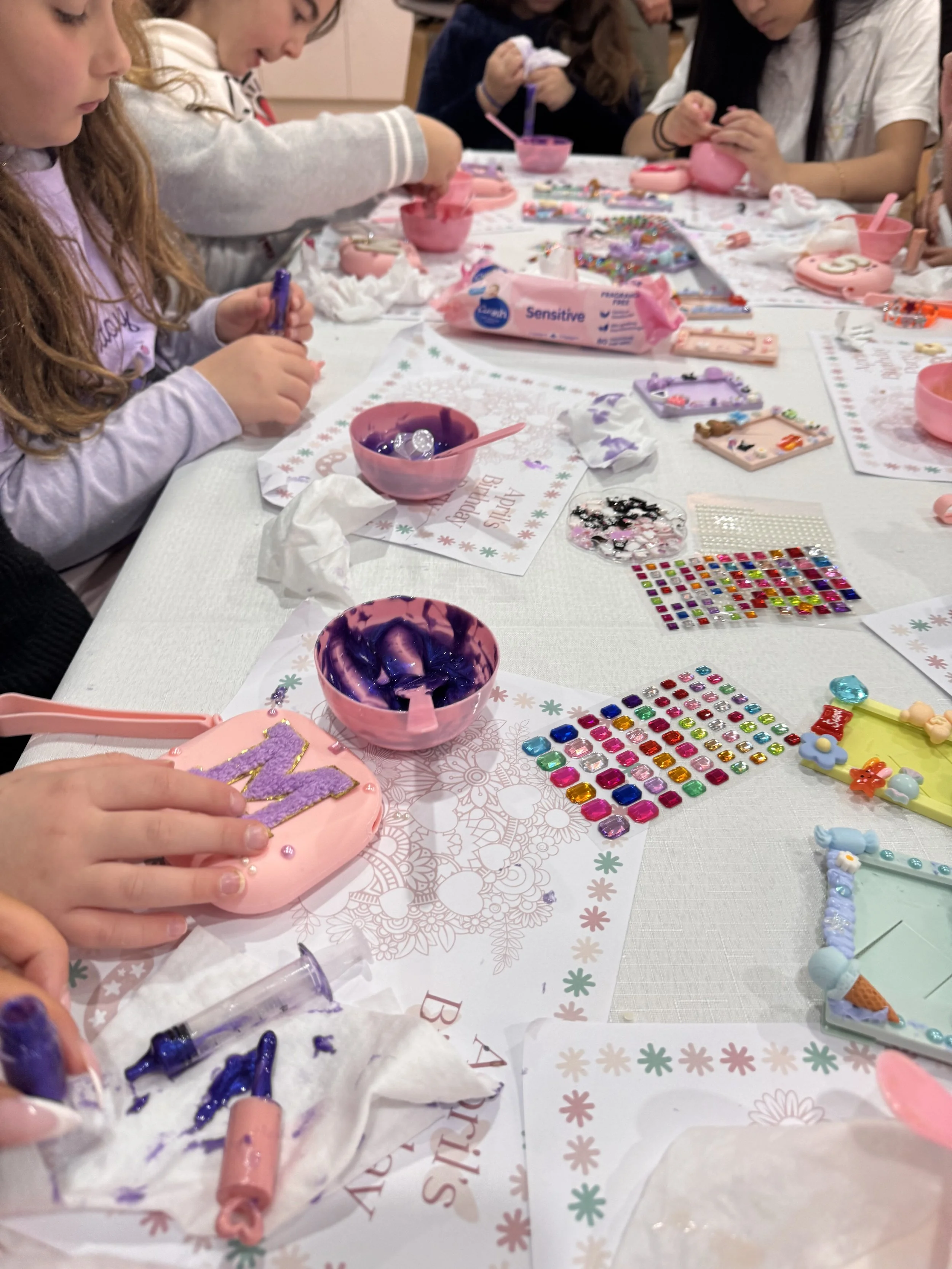 Children decorating cookies at a holiday-themed craft table with various craft supplies and decorations. lip gloss making kids soiree