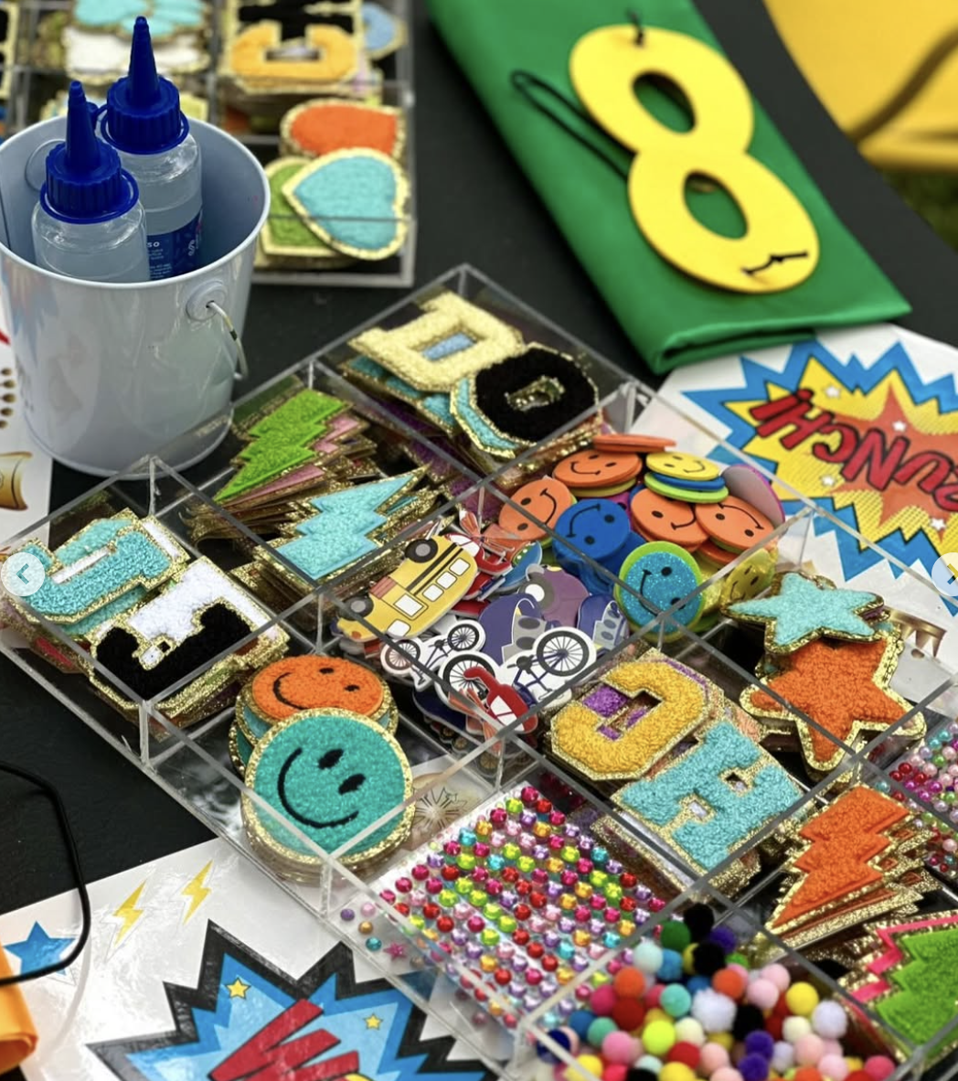 Colorful craft supplies on a table, including decorated patches, buttons, pom-poms, glue bottles, and a green fabric with the number 8. kids soiree craft activity parties