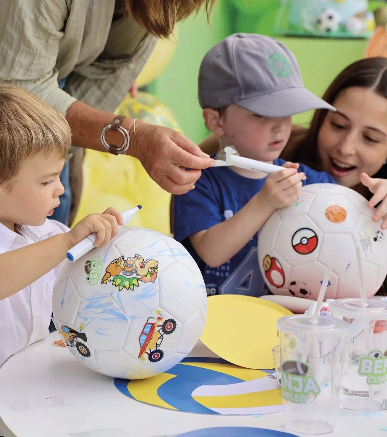 Children and an adult decorating soccer balls with markers at a table. kids soiree soccer ball party