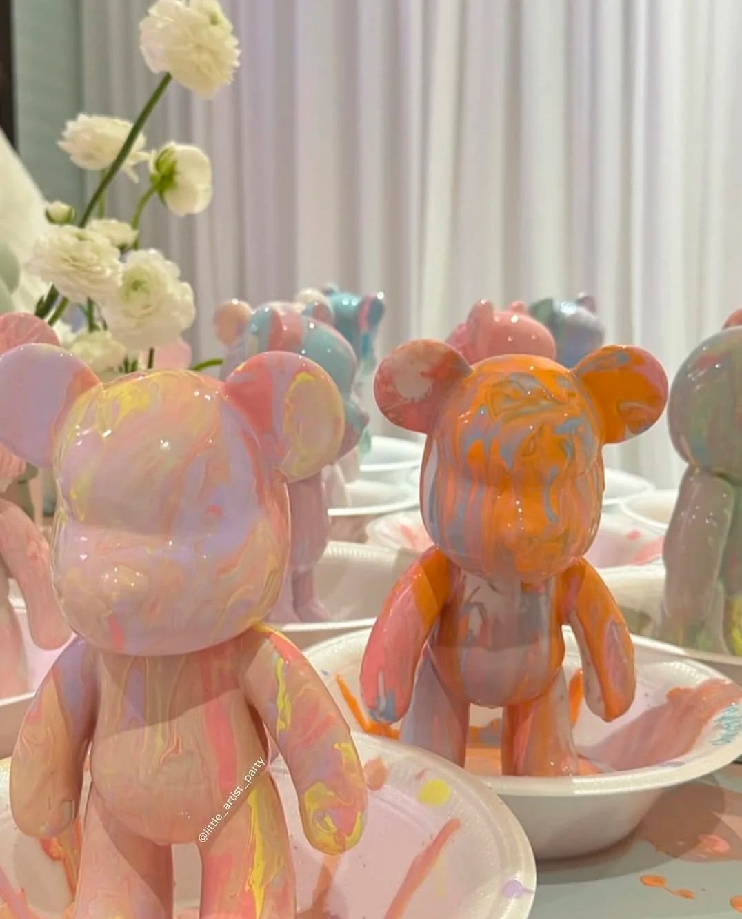 Colorful teddy bear-shaped cakes with pastel swirls on display, with white flowers in the background. kids soiree craft activity parties