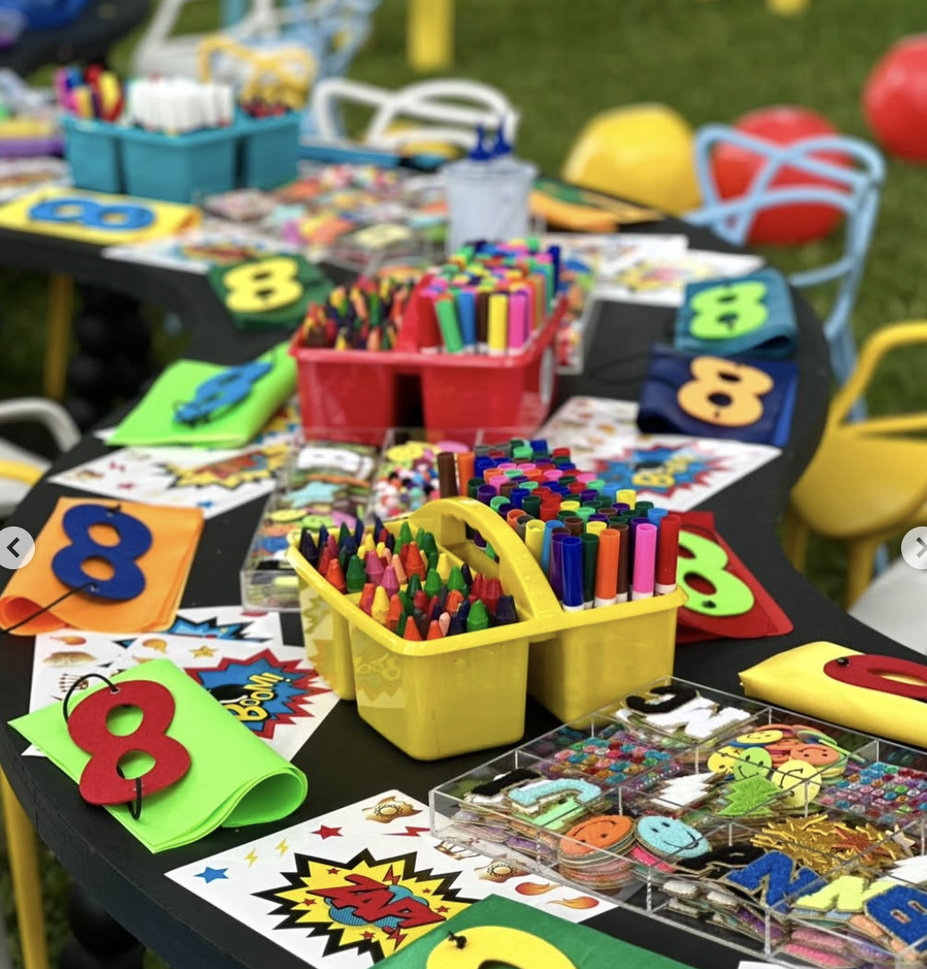Colorful craft supplies, including markers, foam numbers, and stickers, on a black table at an outdoor event. kids soiree craft activity parties