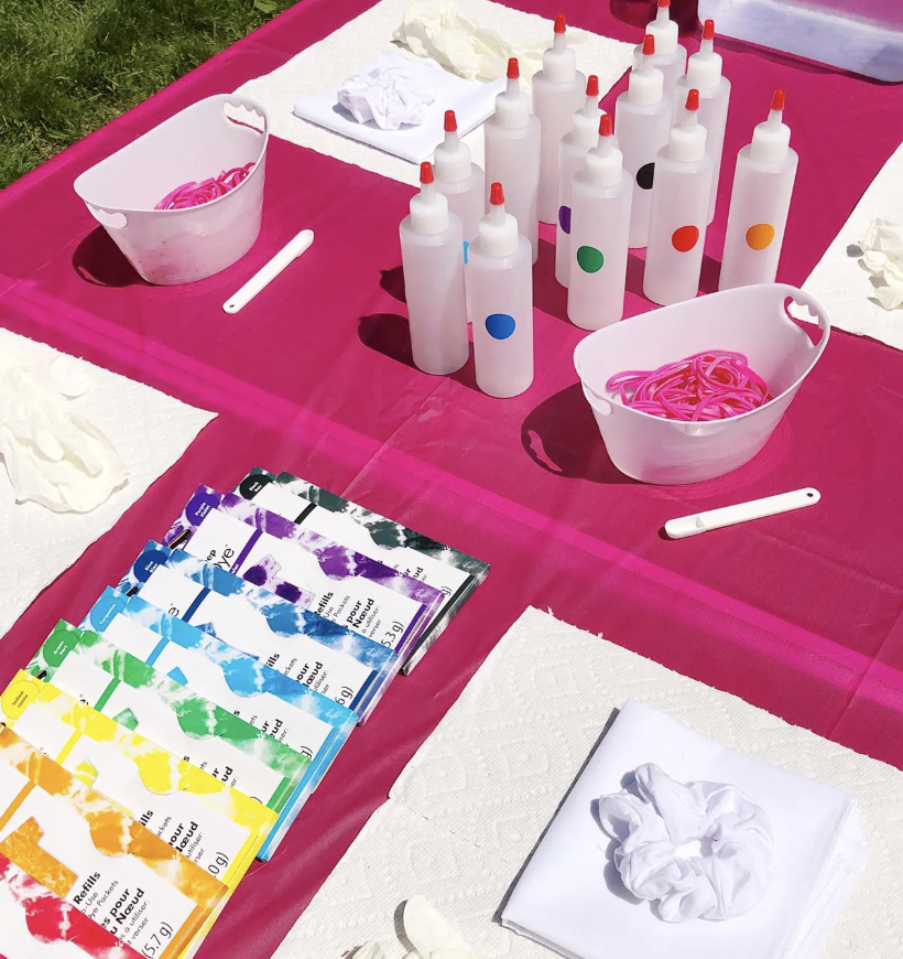 A table set up for tie-dyeing with white bottles of dye, rubber bands, and gloves, along with color swatches and paper towels. kids soiree craft activity parties