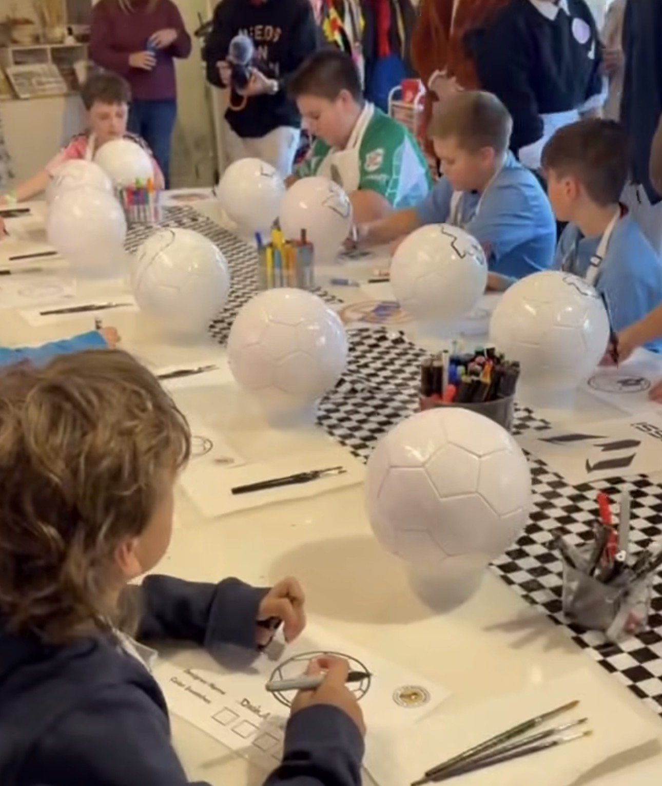 Children seated around a table decorating paper lanterns resembling soccer balls in a classroom or craft area. kids Soiree soccer party