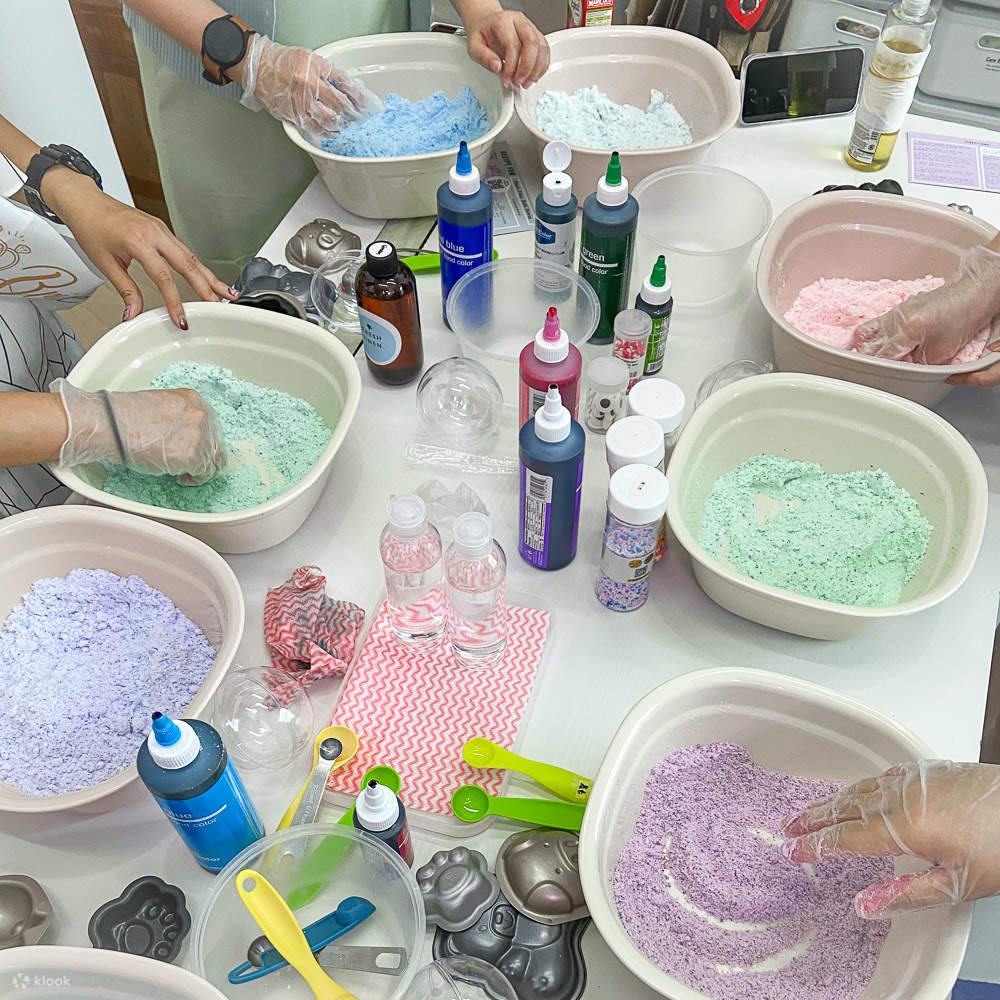 People making bath bombs with colorful powders, liquids, and molds on a table in a workshop. kids soiree craft activity parties