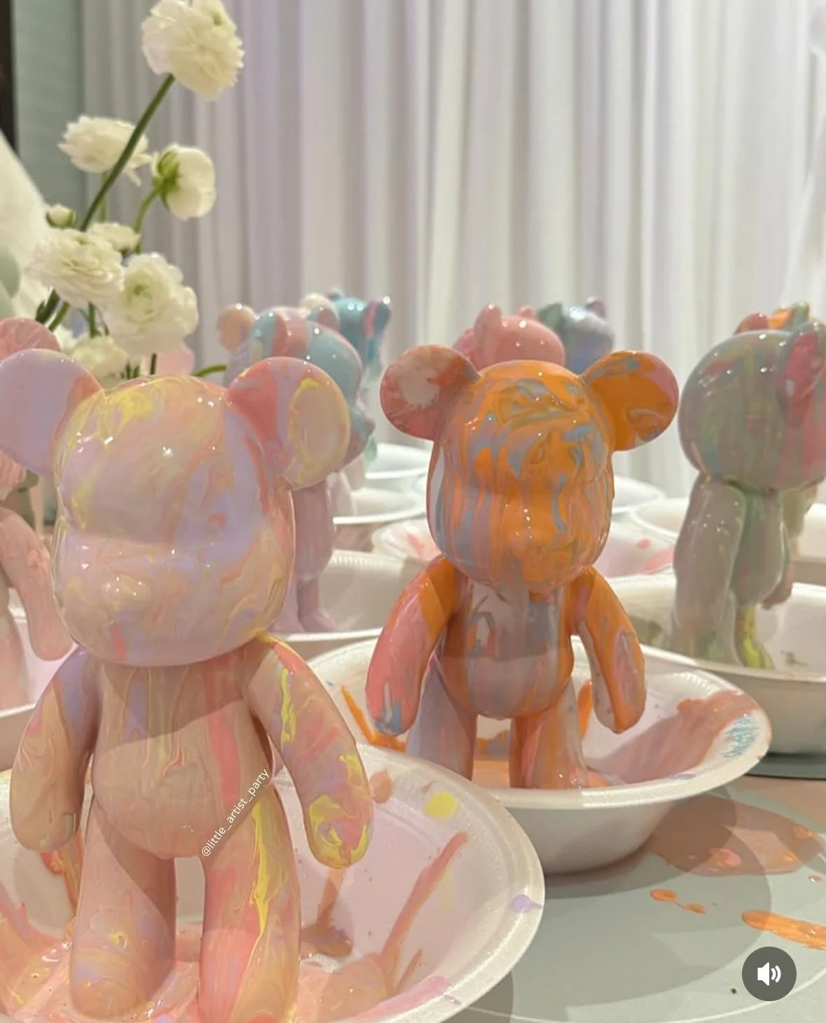 Colorful marble-patterned teddy bear sculptures on white plates, with white flowers in the background. kids soiree craft activity parties