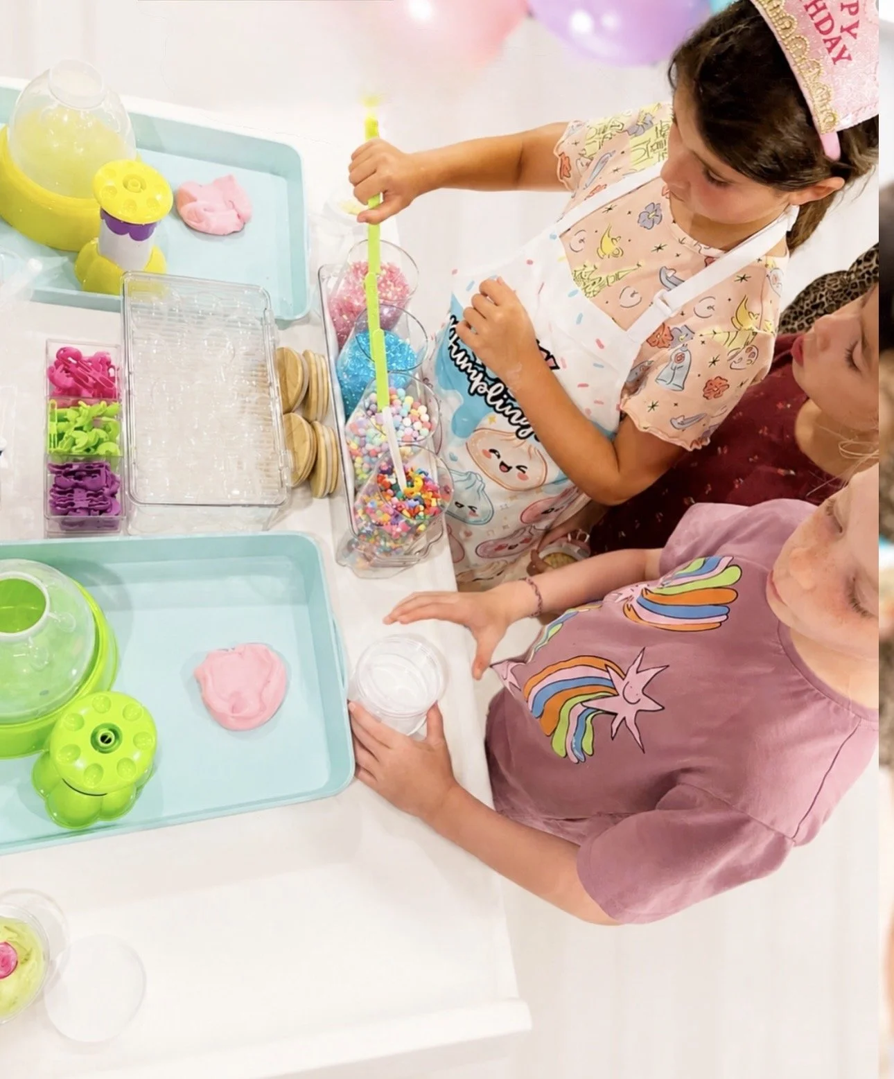 Two children at a birthday party preparing to make slime with various colorful ingredients and tools on a table. kids soiree craft activity parties