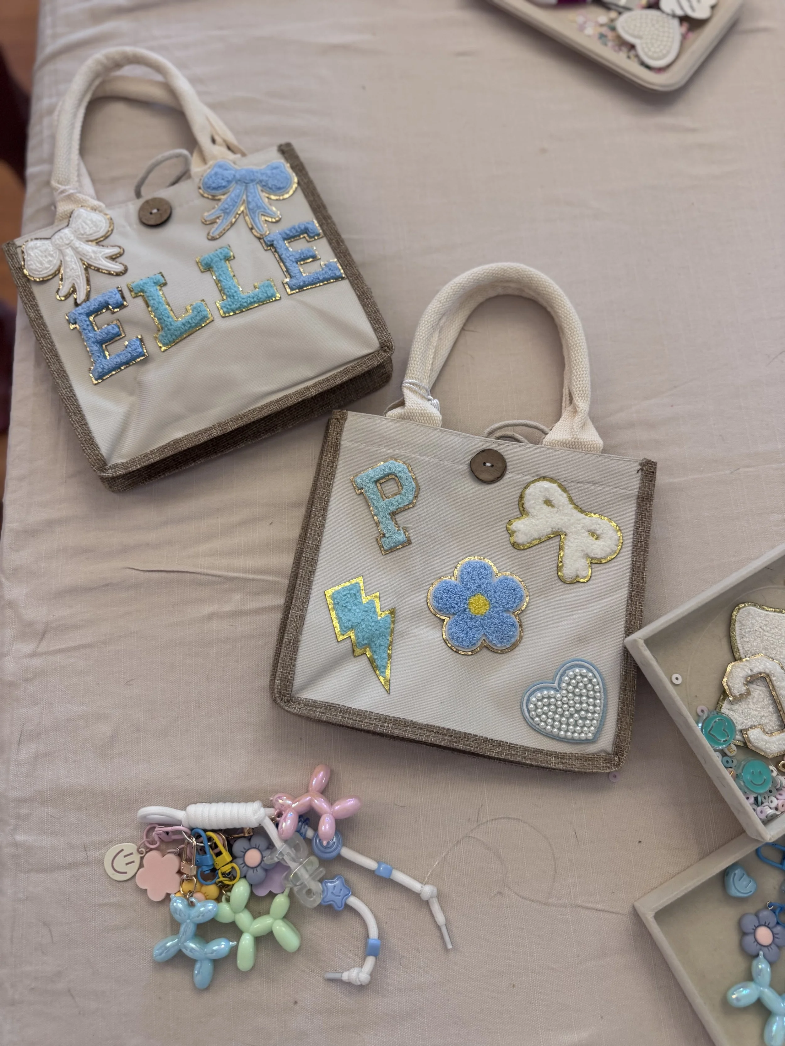 Colorful embroidered patches and accessories with designs of flowers, lightning bolts, hearts, and other shapes on fabric pouches, along with craft beads and charms on a table. kids soiree craft activity parties
