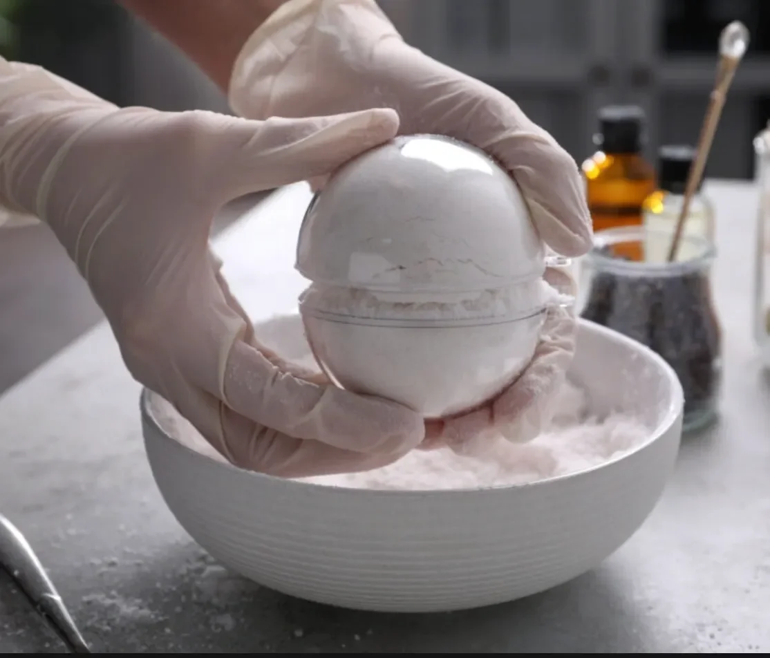 Person wearing gloves holds a decorative white marble sphere over a bowl, with various jars and utensils in the background. kids soiree craft activity parties