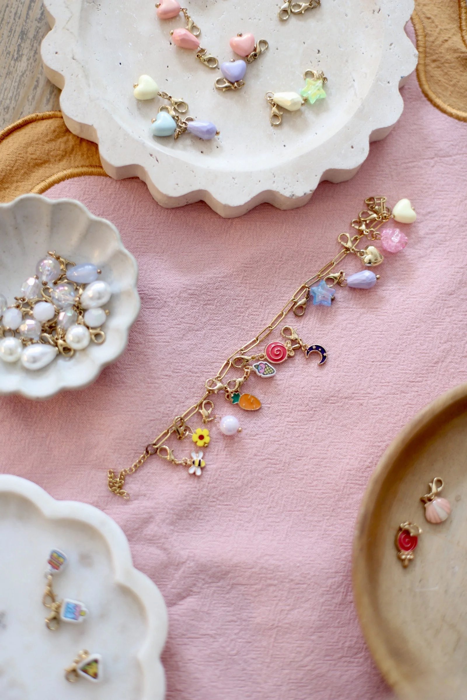 Colorful charms with pastel colors, hearts, stars, and other cute shapes on a pink and beige background with decorative bowls. kids soiree craft activity parties