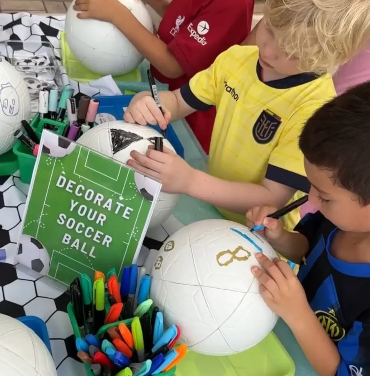 Children decorating soccer balls with markers at a table. kids soiree soccer ball decorating party