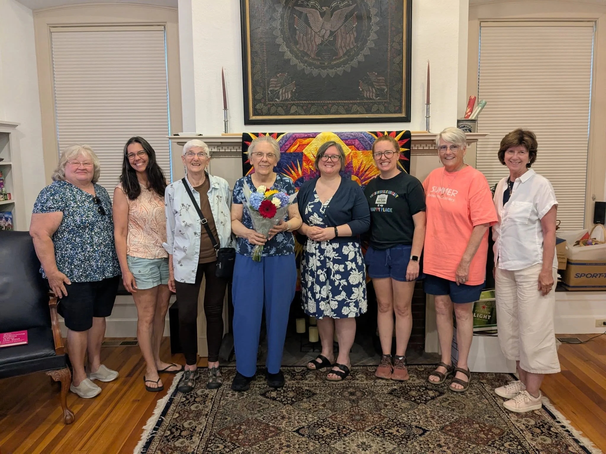 A group of eight women standing in front of the library's historic fireplace.