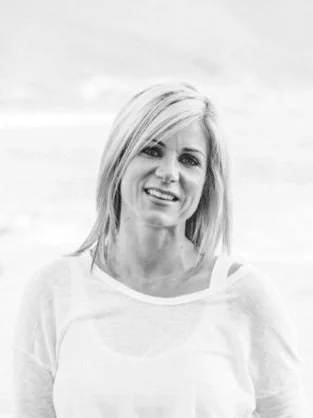 Black and white photo of a woman with shoulder-length blonde hair, smiling, wearing a light-colored top.
