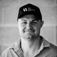 Portrait of a man wearing a black cap and a checkered shirt, smiling gently.