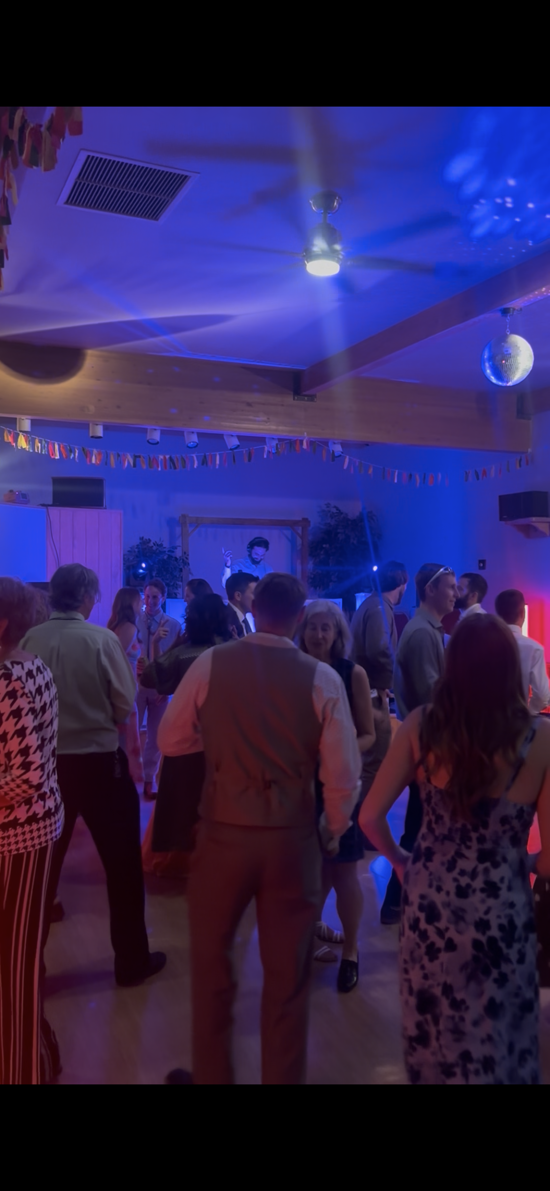 People dancing and socializing at a party with colorful lighting and a disco ball