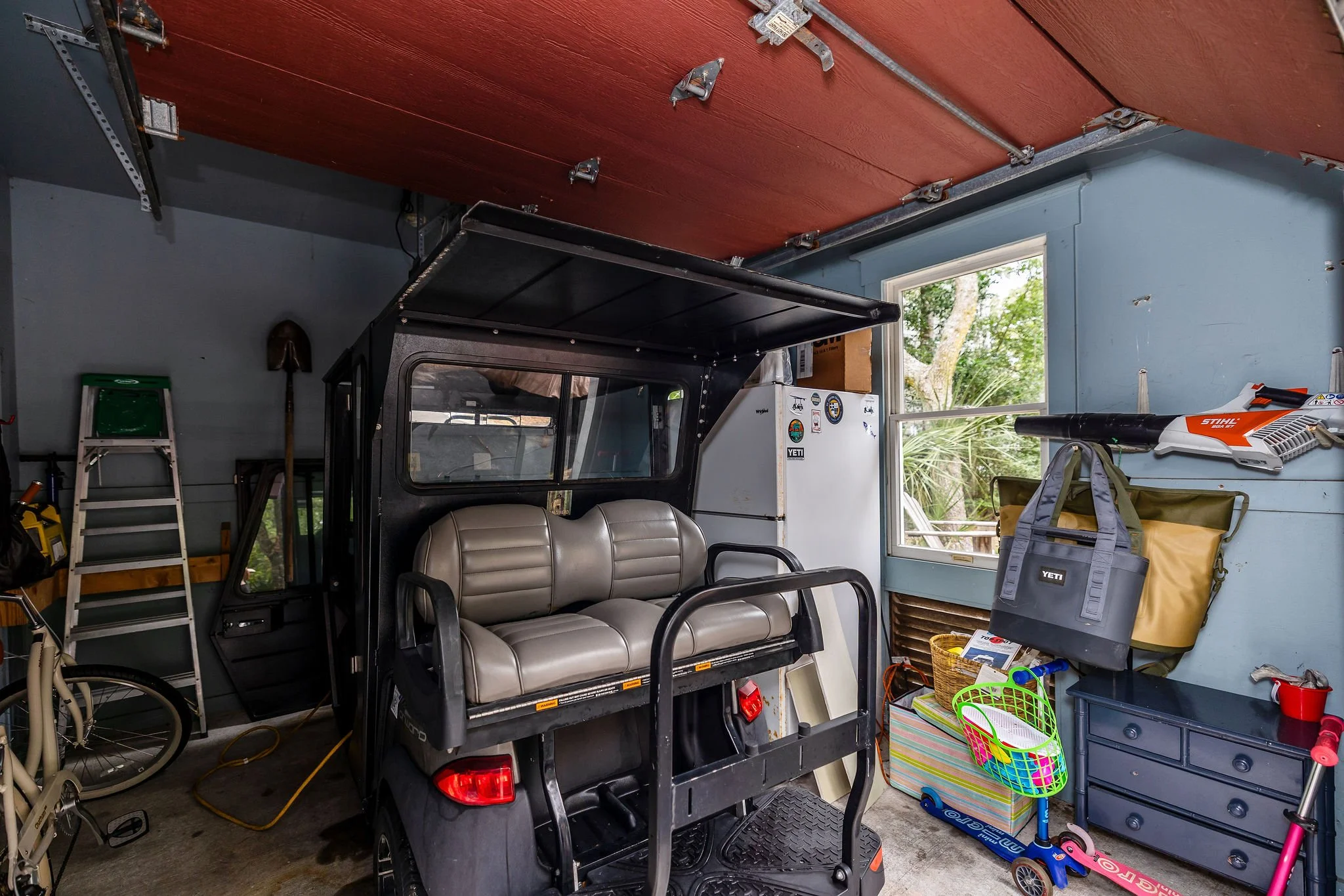 Garage interior with a golf cart, bicycle, tools, storage boxes, and children's toys.