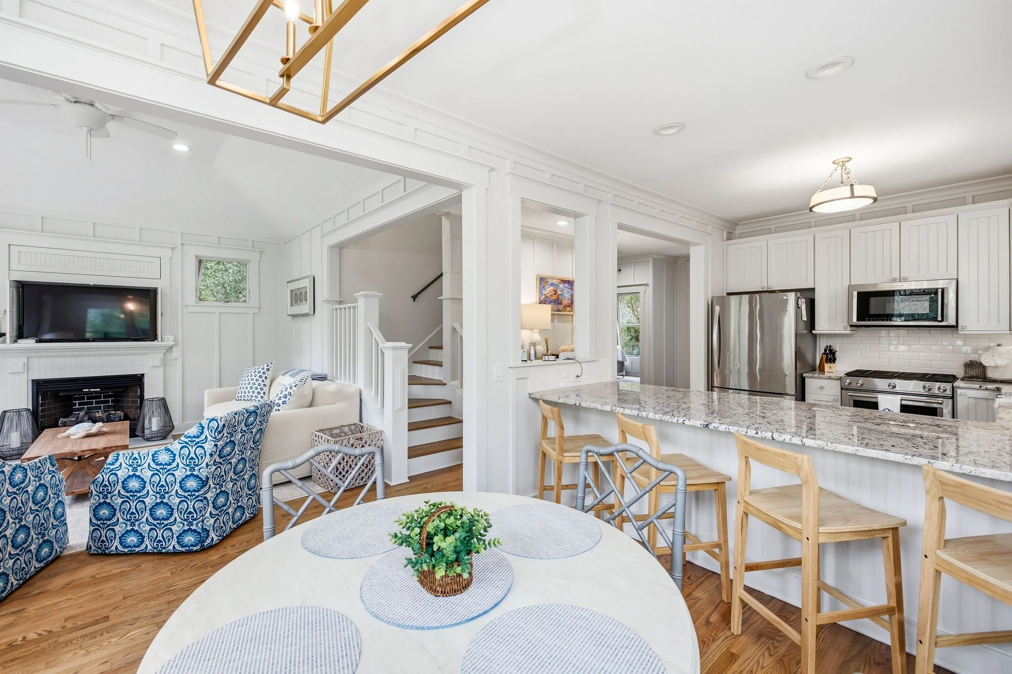 Open-concept living room and kitchen with white cabinetry, granite countertops, stainless steel appliances, a fireplace, and blue patterned armchairs.