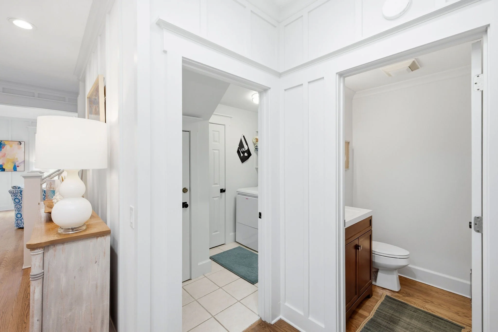 View of a bathroom with door open, showing a toilet, a vanity with a sink, cleaning supplies, and a laundry area with a washing machine.