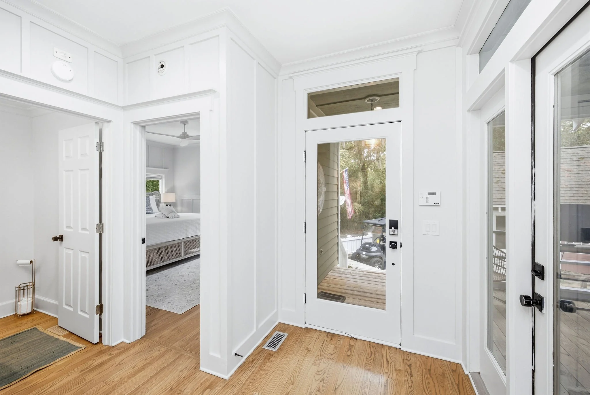 Interior of a modern house entryway with white walls, glass door, and visible bedroom in the background