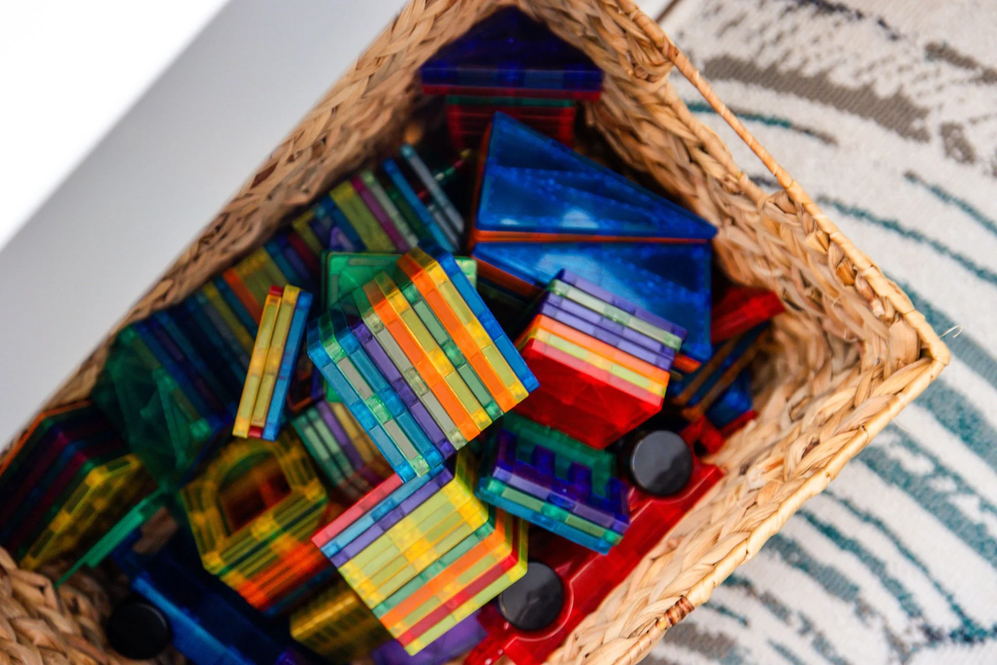 A woven basket filled with colorful glass building blocks, with some black circular pieces visible at the bottom.